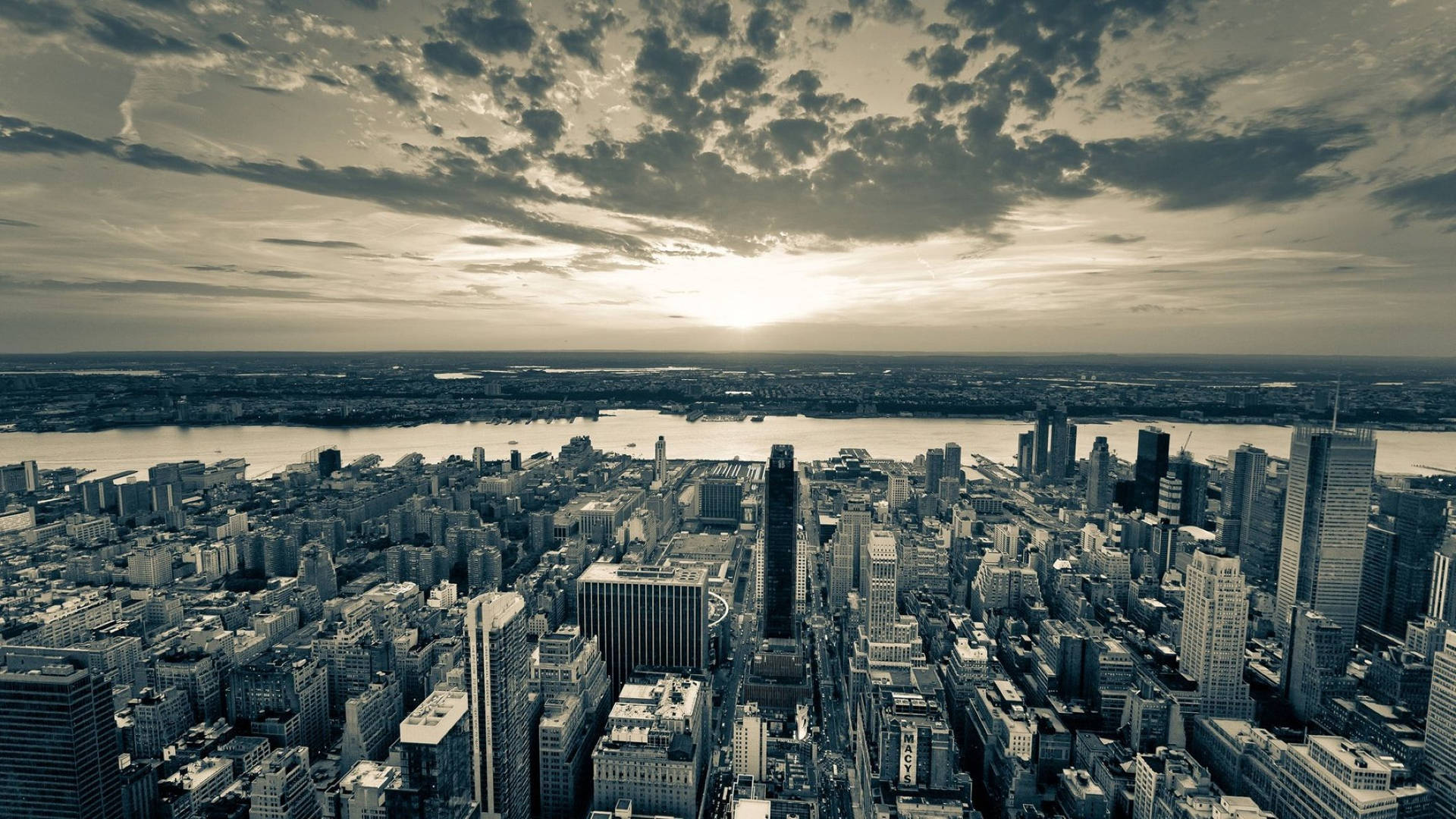 New York 桌布 壁紙 — 一張懷舊色調的鳥瞰圖，展示日落時分密集的城市天際線，雲層在高樓大廈和河流上投下戲劇性的陰影。
