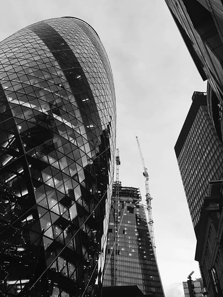 Building 桌布 壁紙 — 一張戲劇性的低角度黑白照片，拍攝了一座彎曲的玻璃摩天大樓，聳立於其他建築物之上，並可見建築起重機。