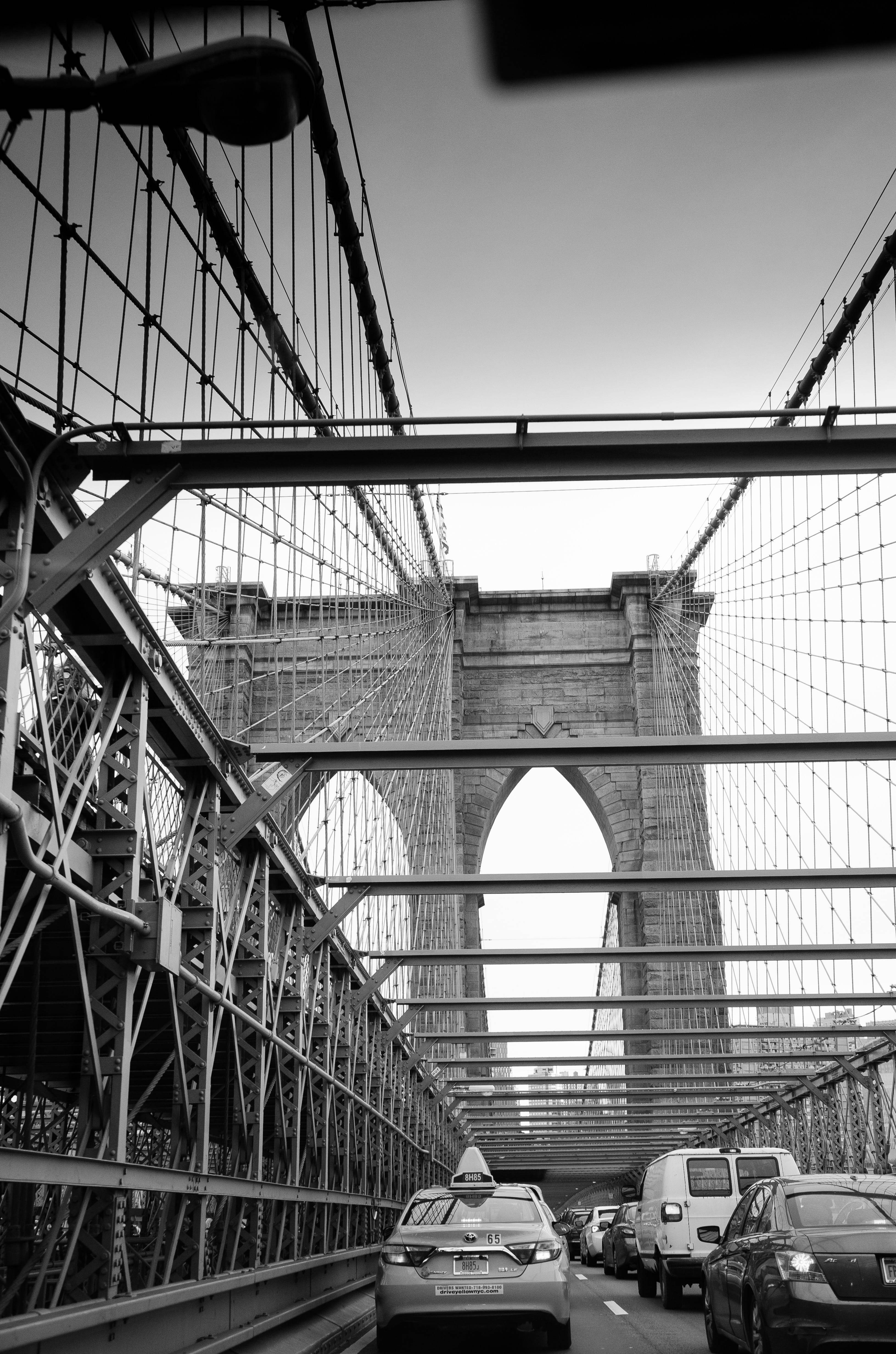 New York 桌布 壁紙 — 一張戲劇性的黑白低角度拍攝布魯克林大橋，汽車在其標誌性石塔和複雜的懸索下移動。
