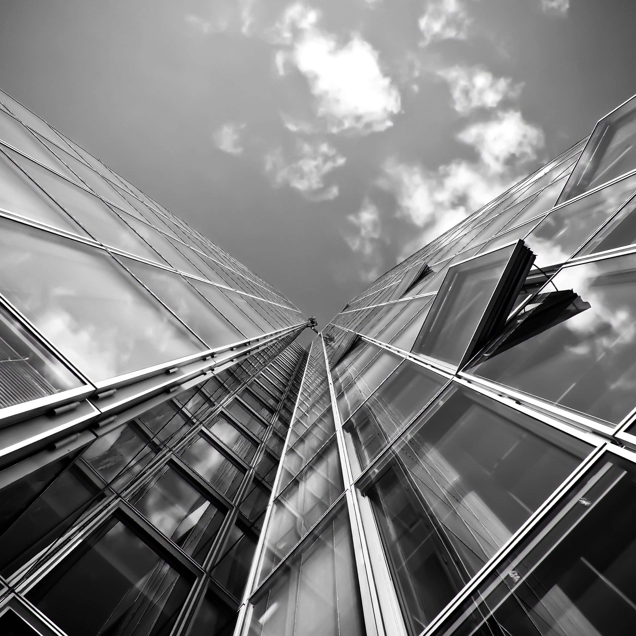Black And White Architecture 桌布 壁紙 — 一張戲劇性的黑白低角度照片，兩座玻璃摩天大樓向多雲的天空匯聚。