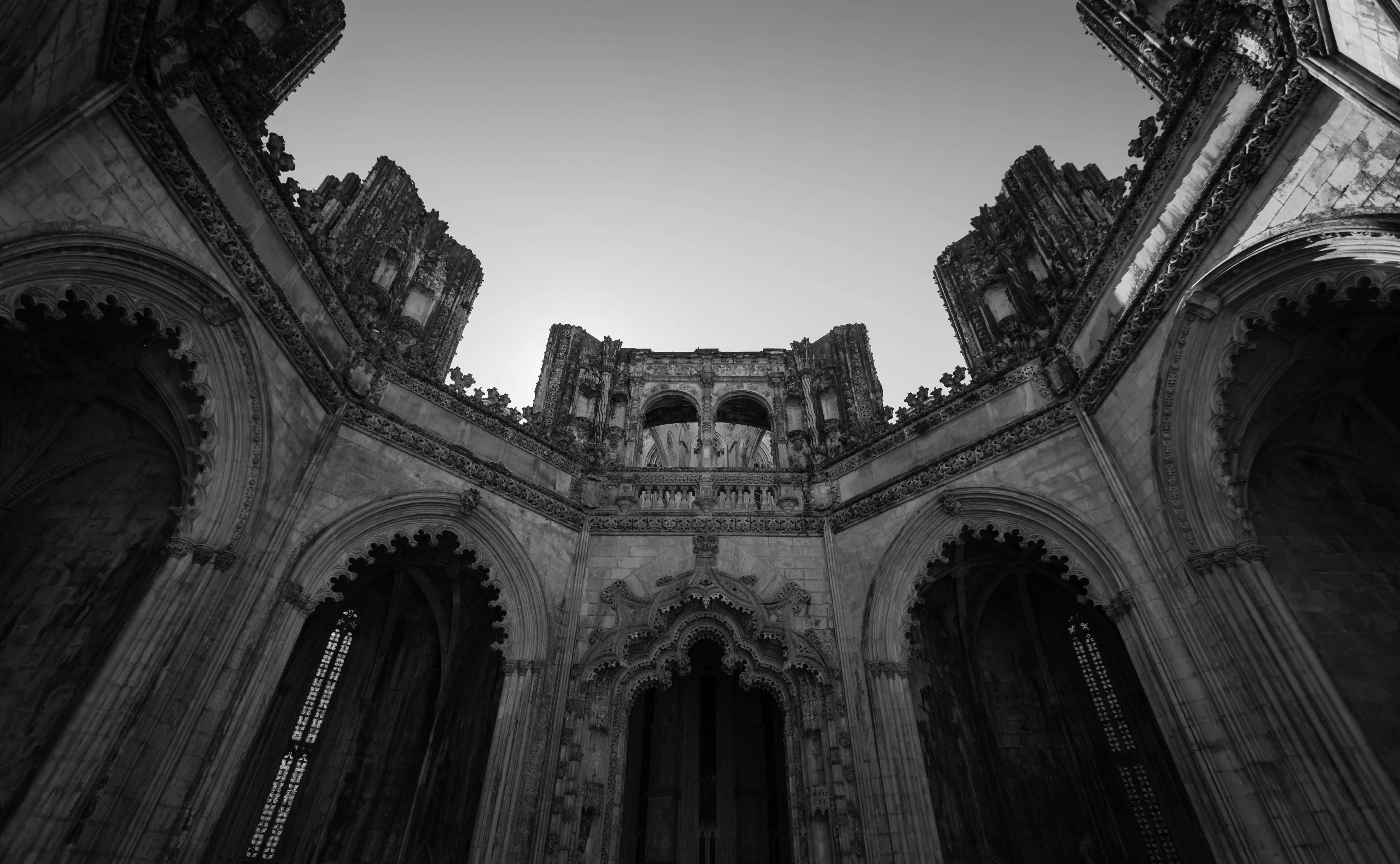 Black And White Architecture 桌布 壁紙 — 一張戲劇性的黑白低角度照片，拍攝了一座廢棄哥德式大教堂精緻的石拱門和拱形天花板，背景是蒼白的天空。