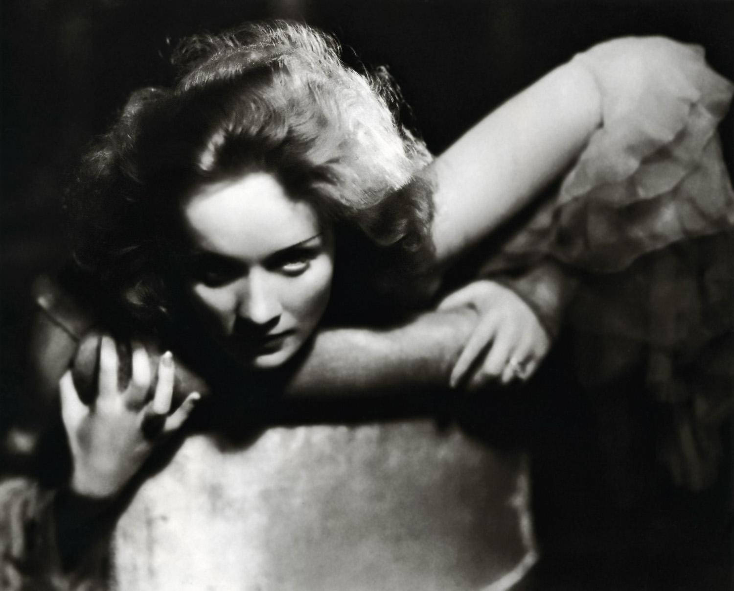 Marlene Dietrich 桌布 壁紙 — 一張戲劇性的黑白肖像，一名頭髮蓬亂的女子以強烈的目光向前傾身。