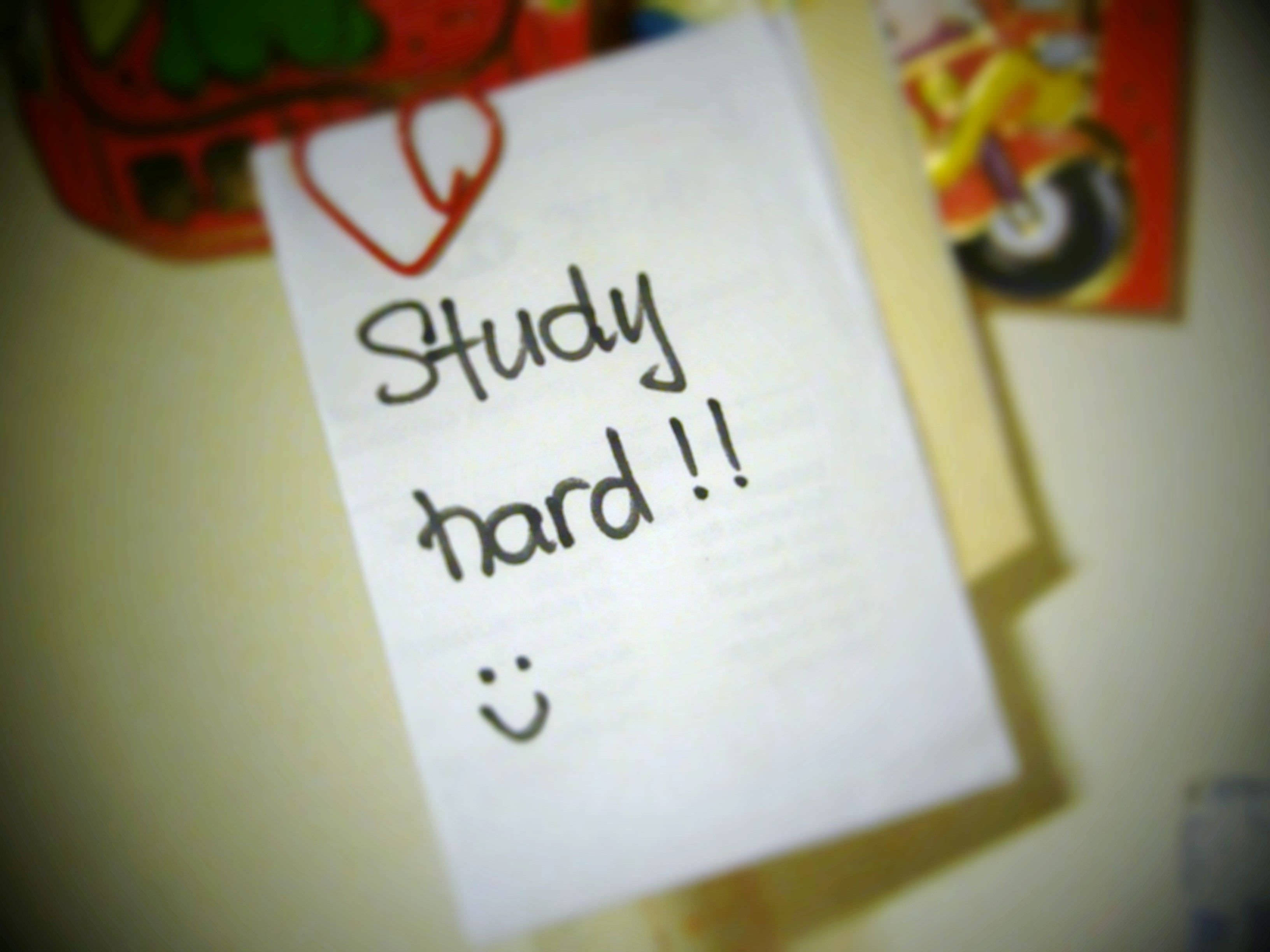 書桌 桌布 壁紙 — 一張手寫便條，上面寫著「Study hard !!」和一個笑臉，用紅色心形夾子固定在牆上。