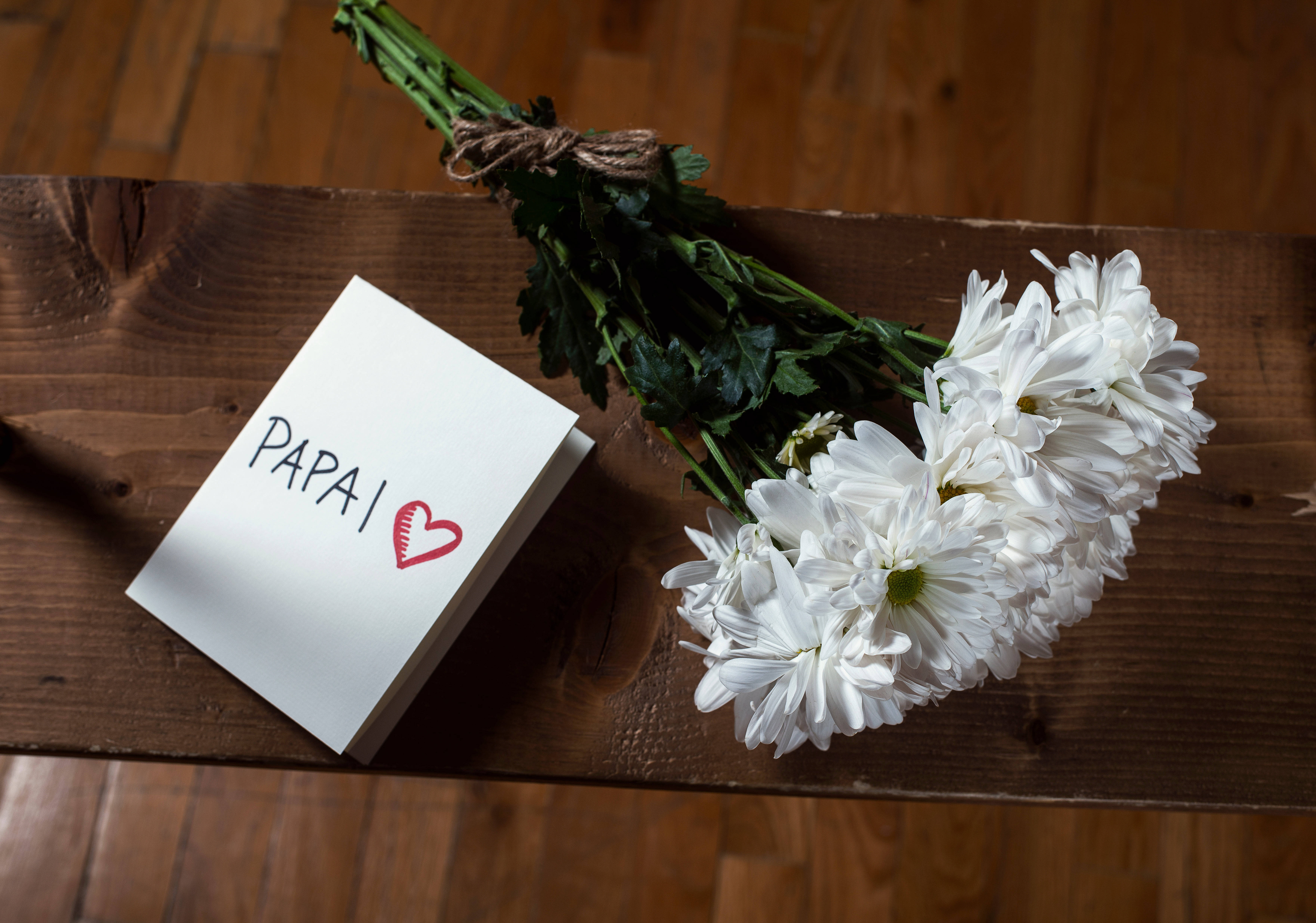 Dad 桌布 壁紙 — 一張手寫便條寫著「PAPAI」並附有一個紅色心形，旁邊放著一束白色菊花，置於鄉村風格的木桌上。