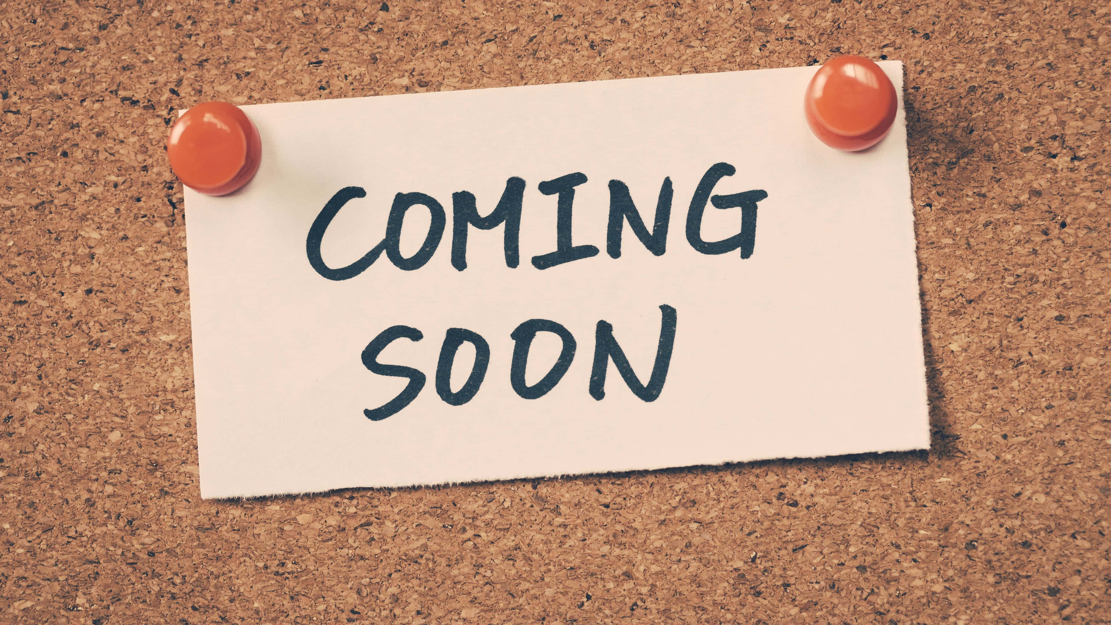 Coming Soon 桌布 壁紙 — 一張手寫便條用大頭針釘在軟木板上，以粗體墨水宣佈「COMING SOON」。