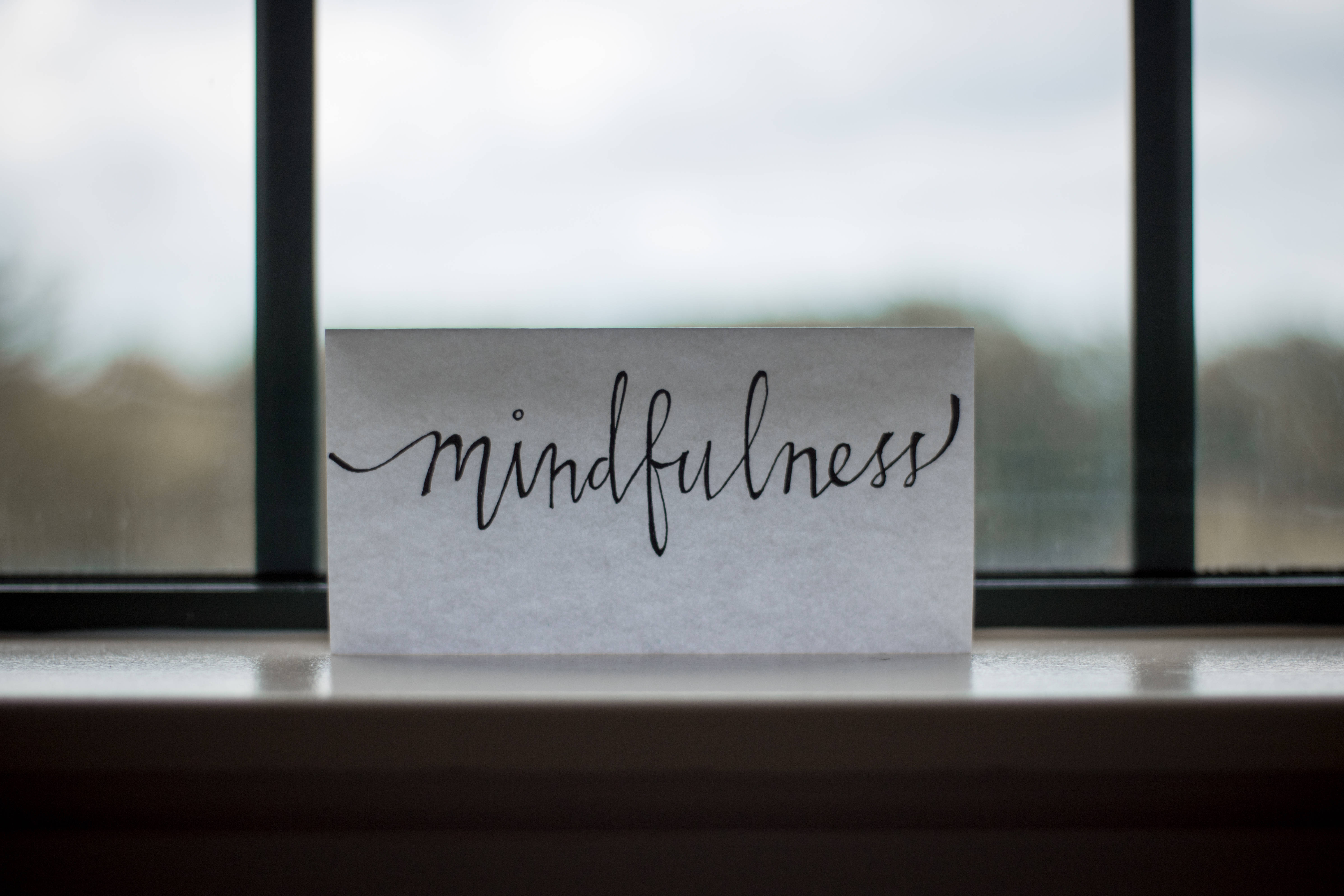 禪 桌布 壁紙 — 一張手寫的正念（mindfulness）便條放在窗台上，背景是模糊的室外景色。