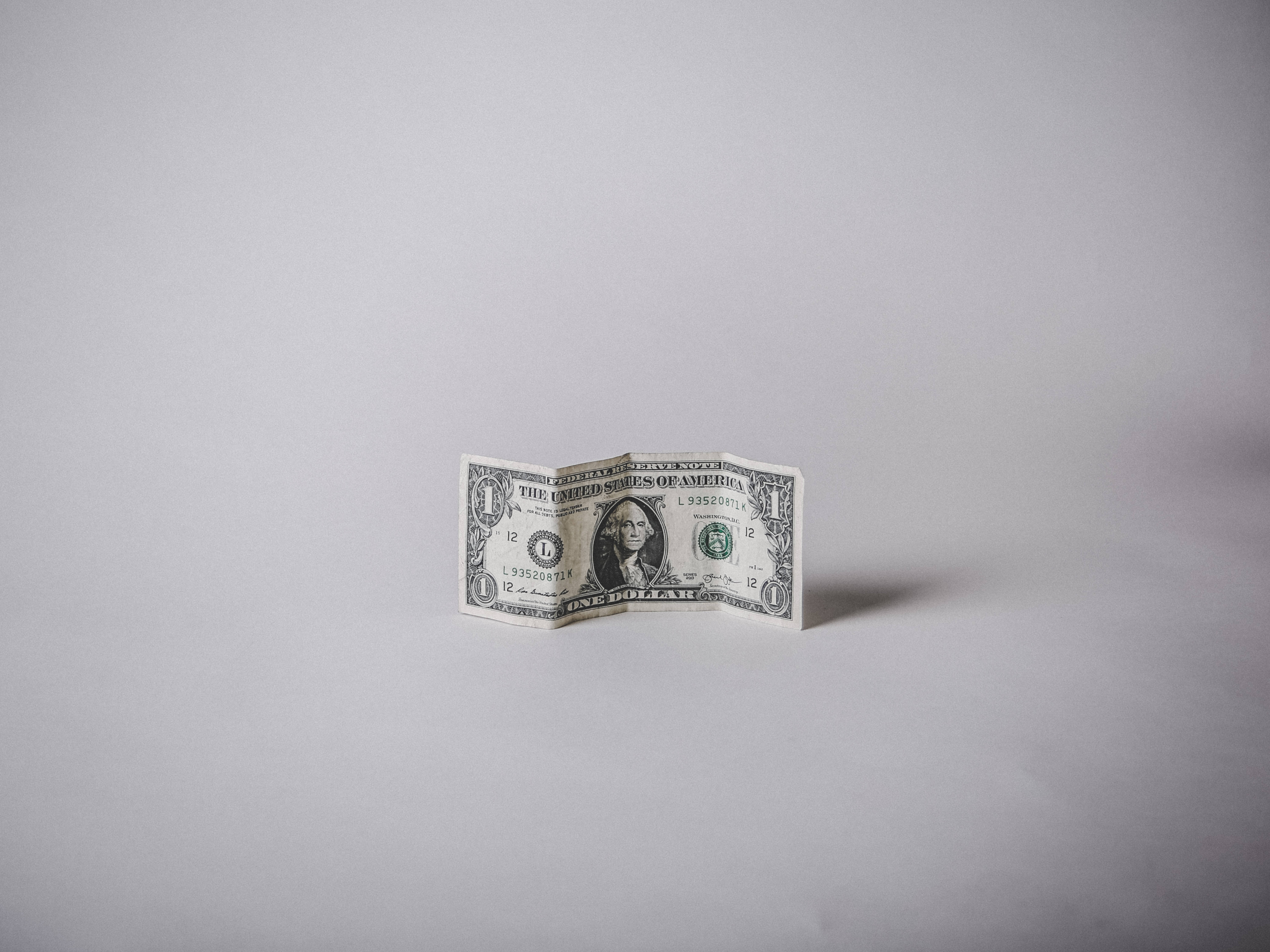 金錢 桌布 壁紙 — 一張折疊的一美元鈔票在柔和的工作室燈光下直立於純灰色表面上。