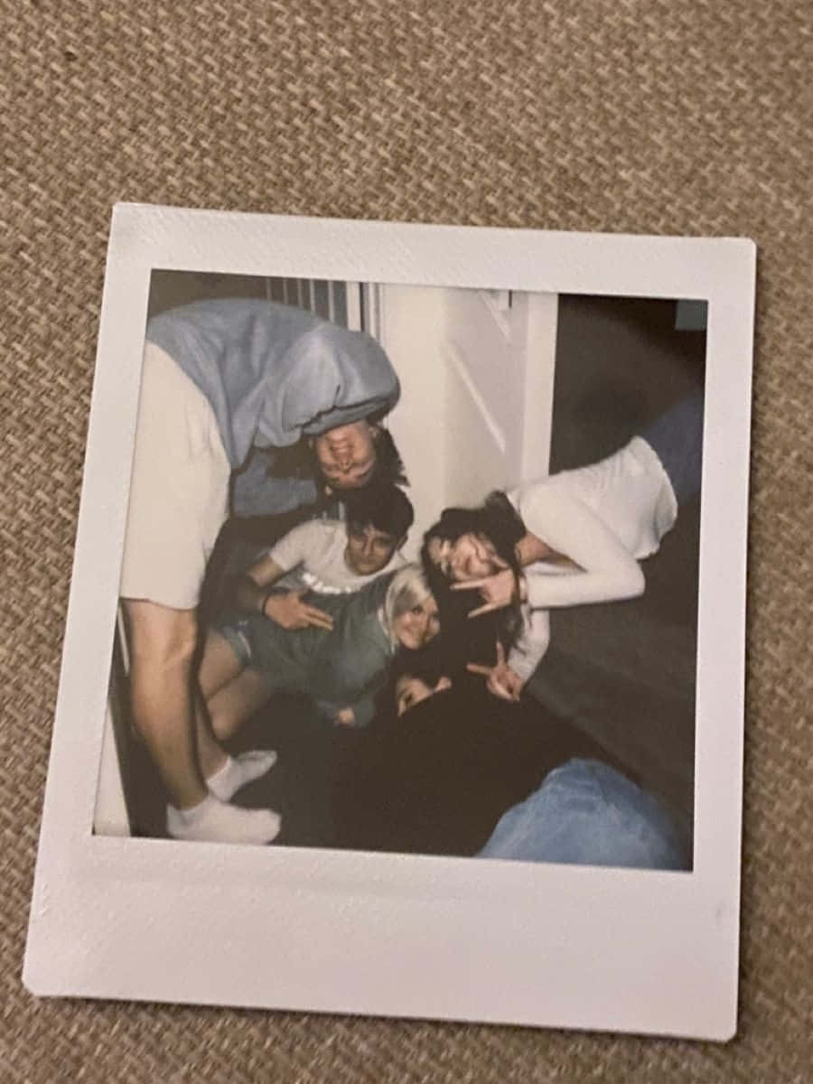 Aesthetic Polaroid 桌布 壁紙 — 一張拍立得照片，四位朋友在鋪有地毯的地板上，以有紋理的米色背景，頑皮地擺姿勢。