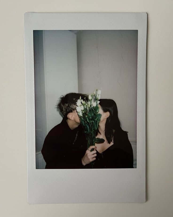 Aesthetic Polaroid 桌布 壁紙 — 一張拍立得照片顯示一對情侶接吻，同時手持一束白色鮮花遮住了他們的臉。