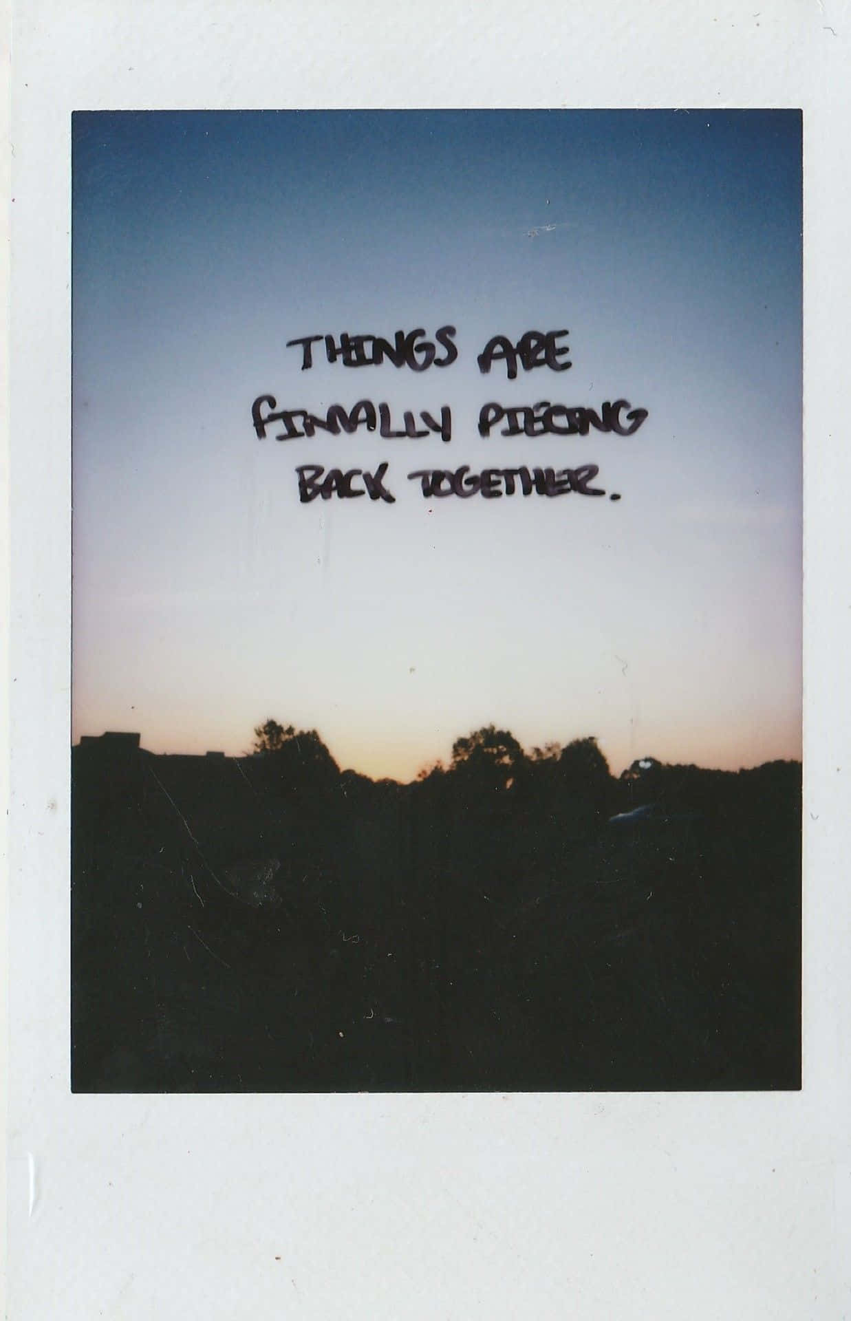 Aesthetic Polaroid 桌布 壁紙 — 一張拍立得風格的照片顯示了暮色天空，手寫文字寫著「事情終於重新拼湊起來」，背景是剪影般的樹木和屋頂。