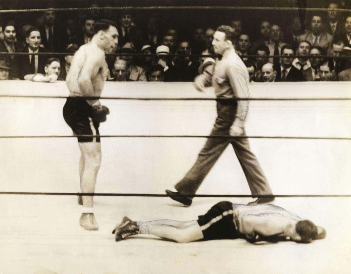 Boxing 桌布 壁紙 — 一張拳擊比賽的復古黑白照片，一名拳手倒在擂台上，裁判和對手站在他上方。