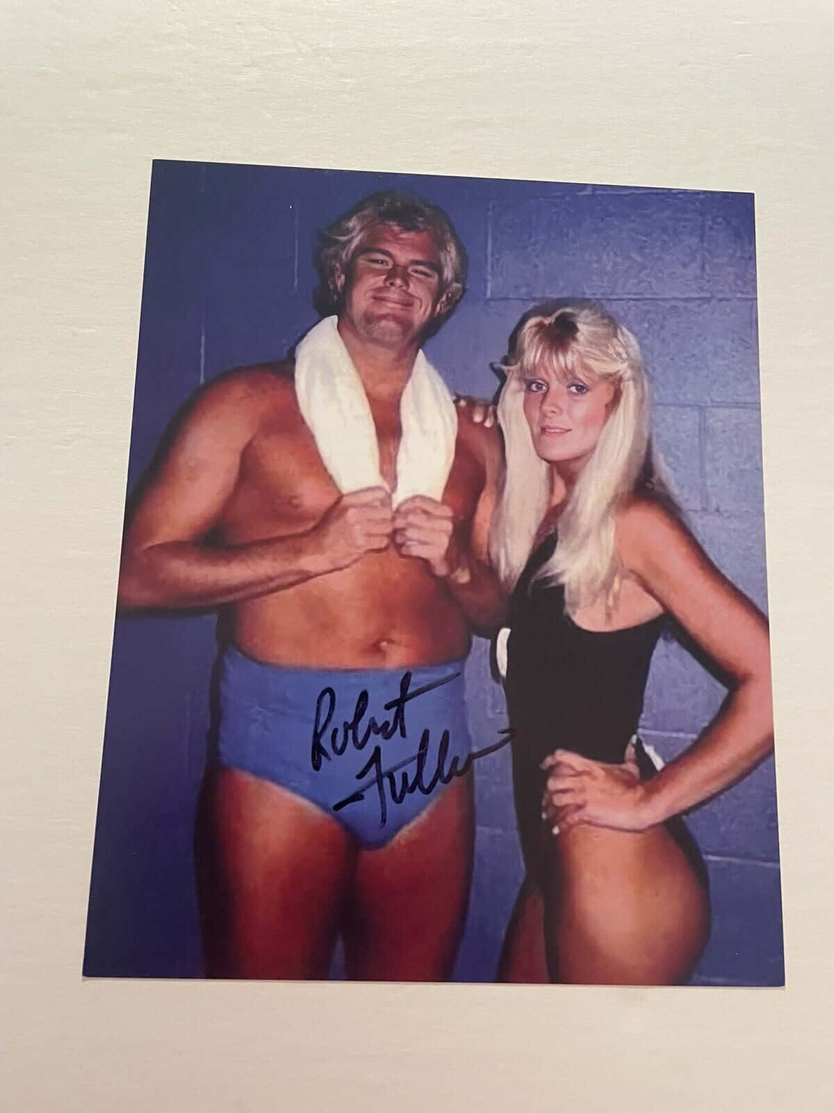 Retro 桌布 壁紙 — 一張摔角手 Robert Fuller 與一位金髮女子在藍色煤渣磚牆前擺姿勢的簽名照片。