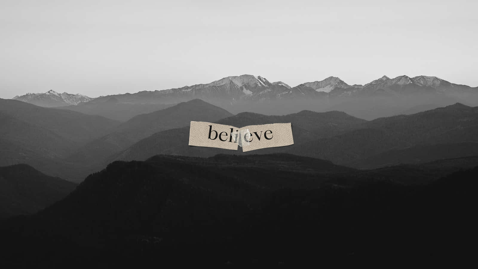 Aesthetic Black And White 桌布 壁紙 — 一張撕破的紙上寫著「believe」，漂浮在單色風景中層疊的山脈之上。