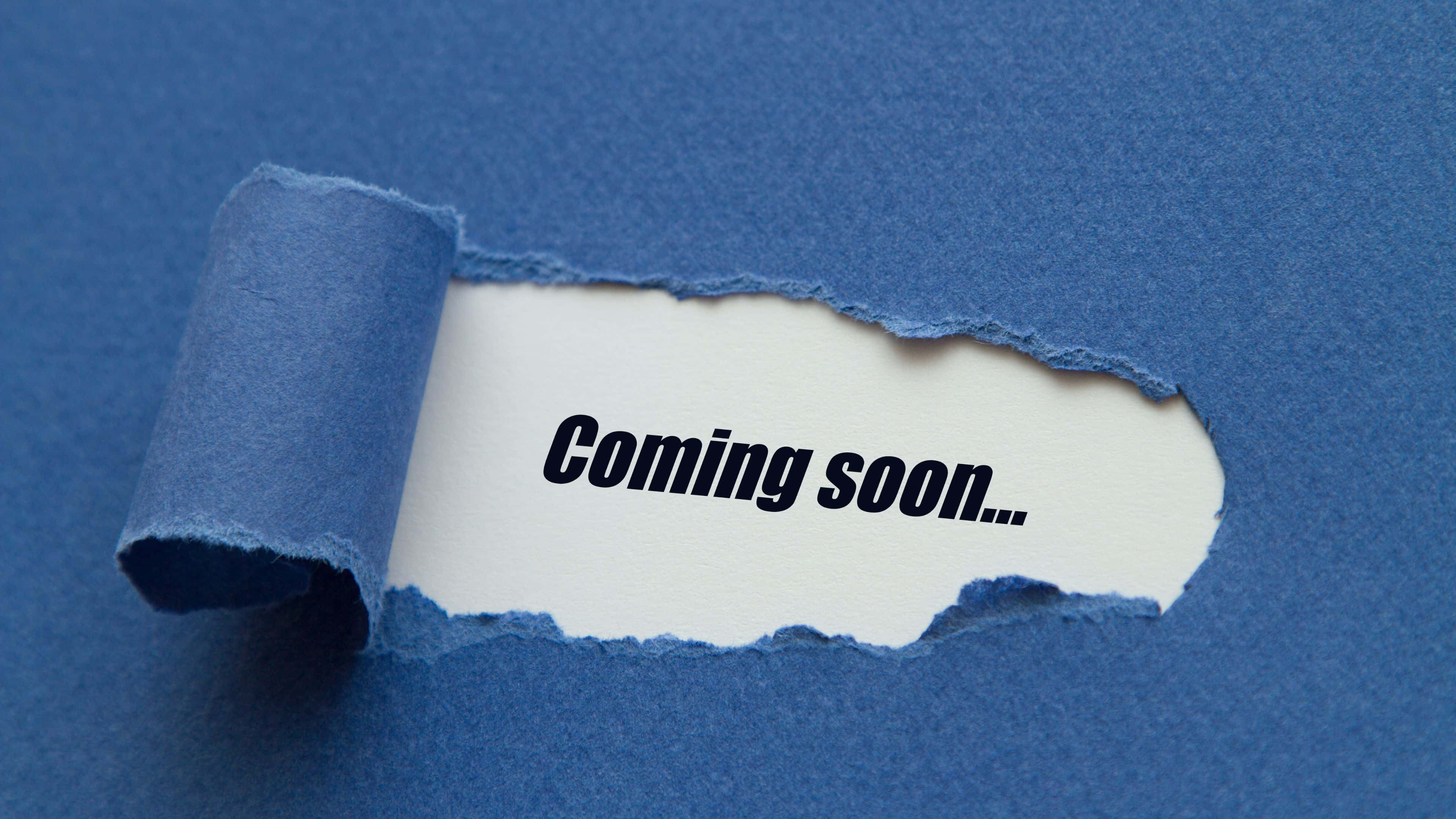 Coming Soon 桌布 壁紙 — 一張撕破的藍色紙張露出一條白色條紋，上面以粗體黑色字體寫著「Coming soon...」。