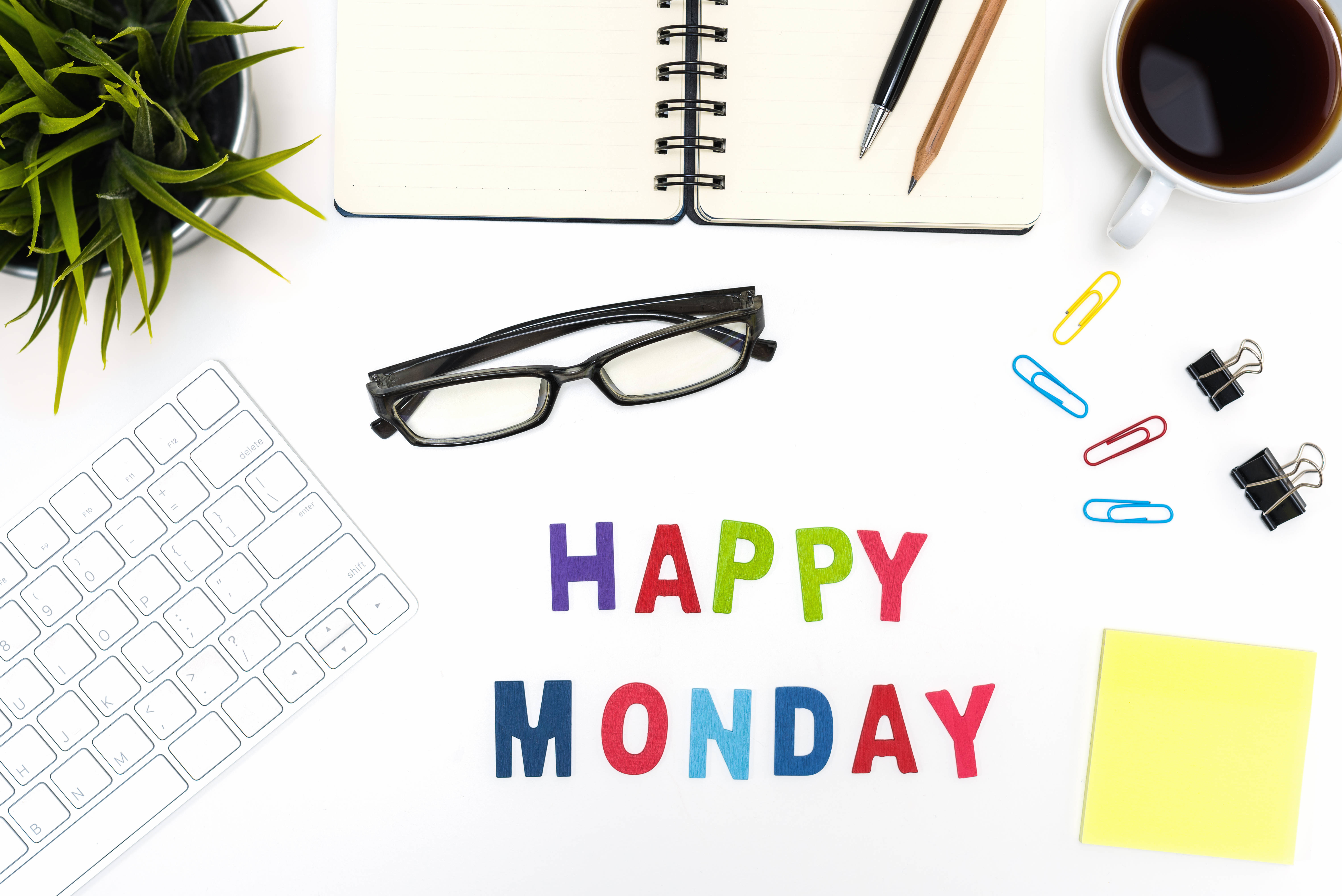 Happy Monday 桌布 壁紙 — 一張明亮的白色桌子上放著色彩繽紛的「HAPPY MONDAY」字母，周圍環繞著鍵盤、眼鏡、咖啡杯和辦公用品。