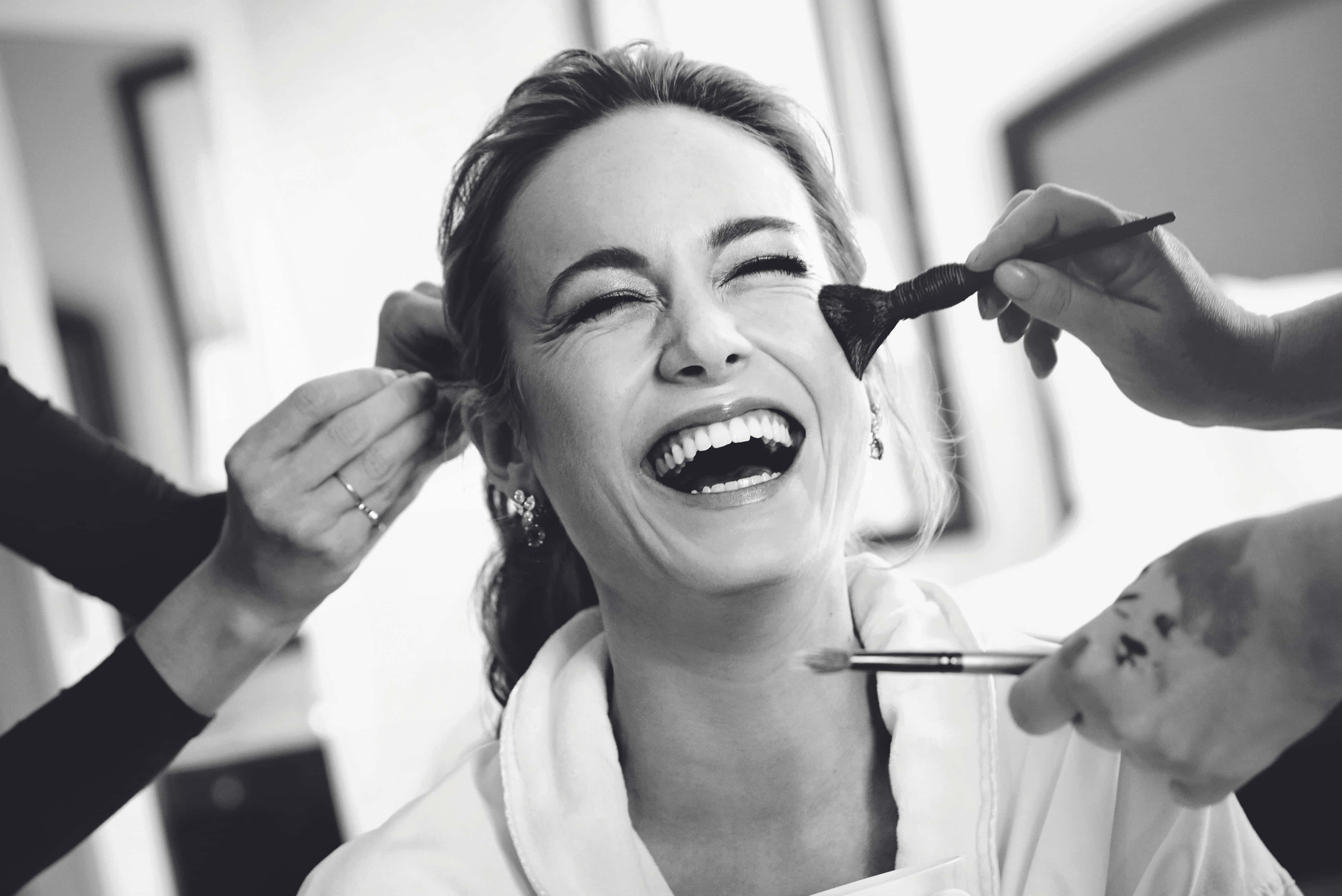 brie larson 桌布 壁紙 — 一張明亮黑白照片中，一位快樂的女性在化妝師為她化妝時開懷大笑。