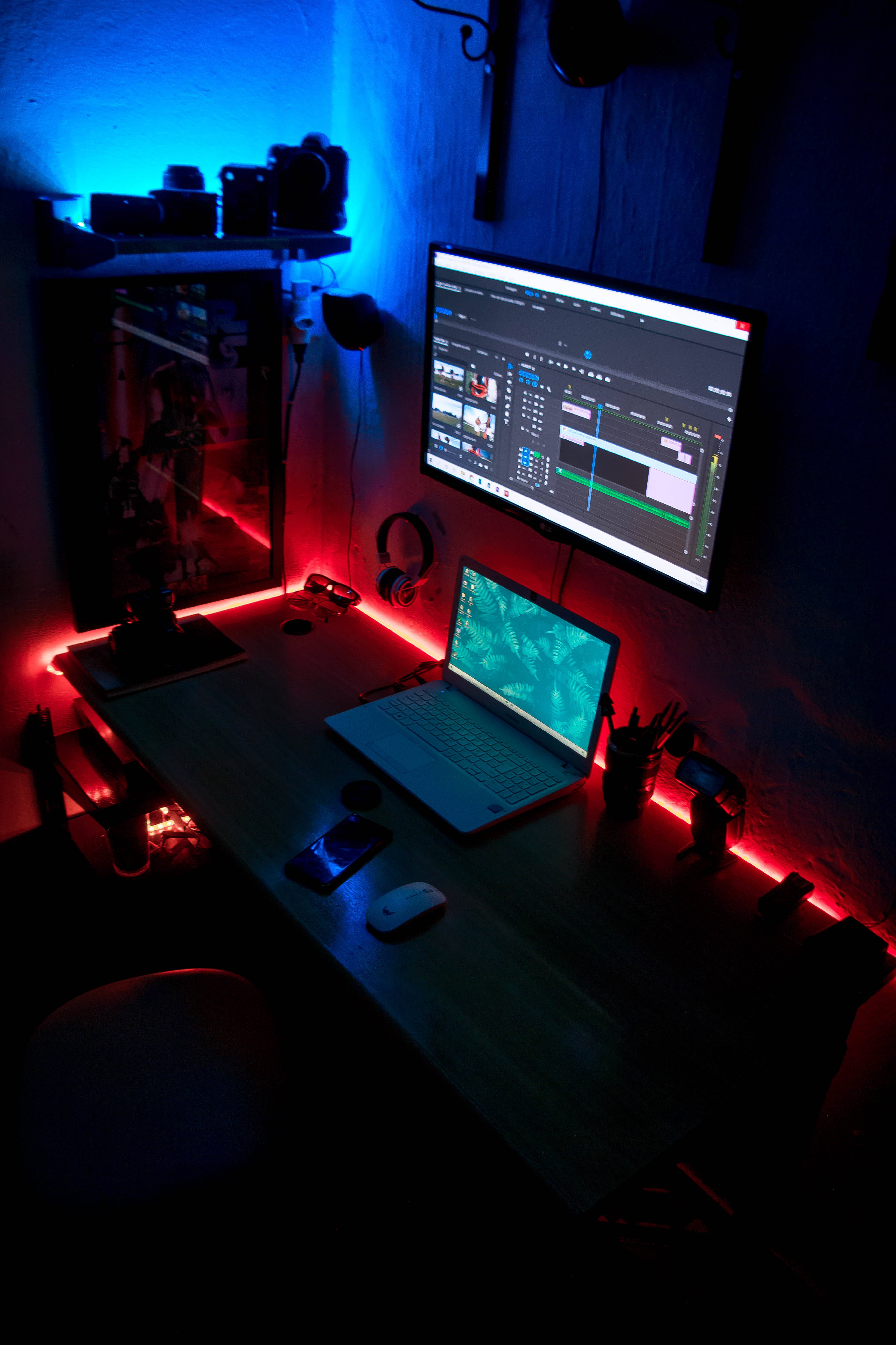 aesthetic tumblr laptop 桌布 壁紙 — 一張昏暗的書桌沐浴在紅色和藍色LED光芒中，桌上放著筆記型電腦和顯示器，顯示著影片編輯軟體。