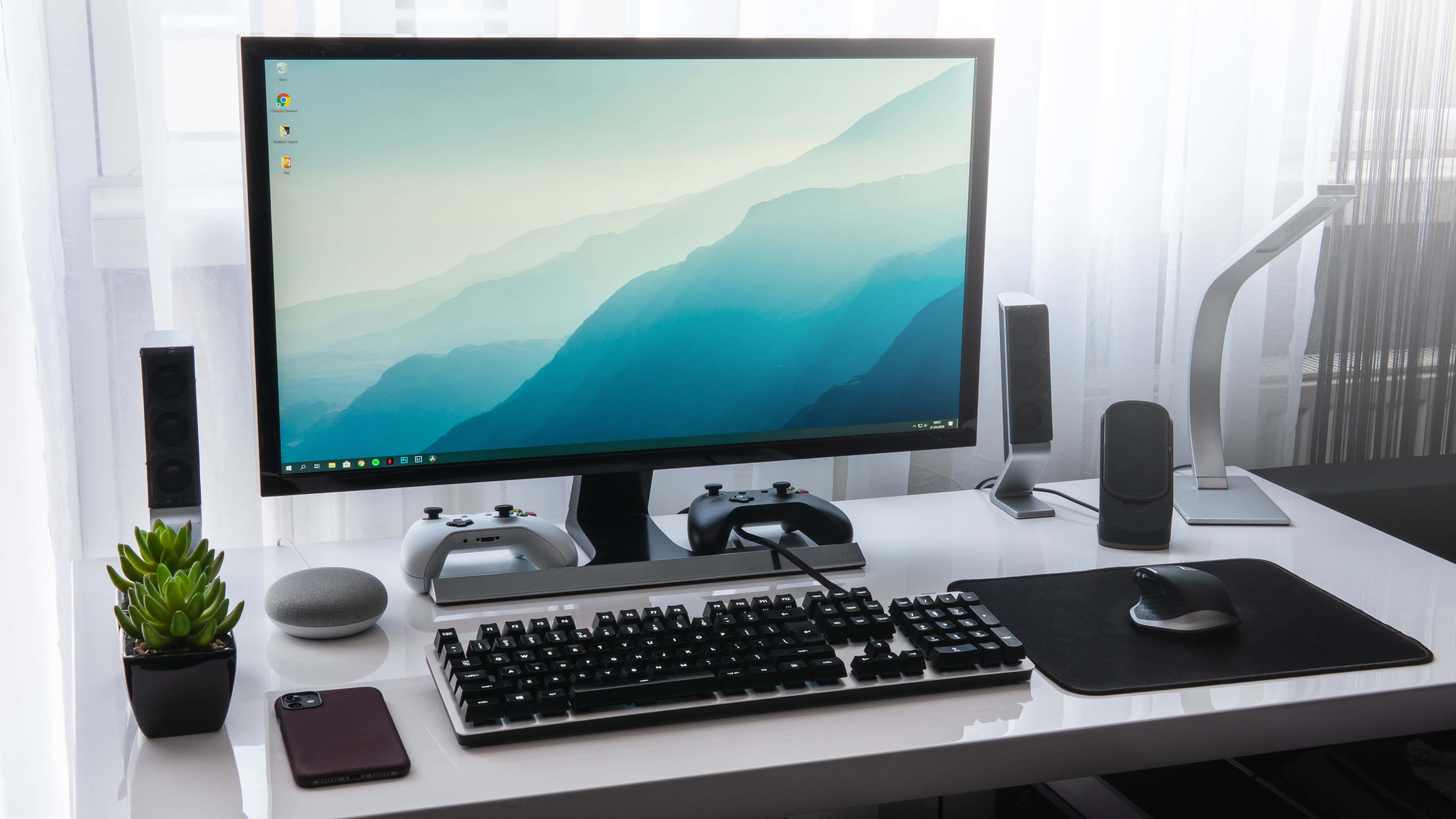 Monitor 桌布 壁紙 — 一張時尚的白色桌子上放著一個顯示器，顯示著山脈壁紙，兩側是揚聲器、遊戲控制器和一盆多肉植物。