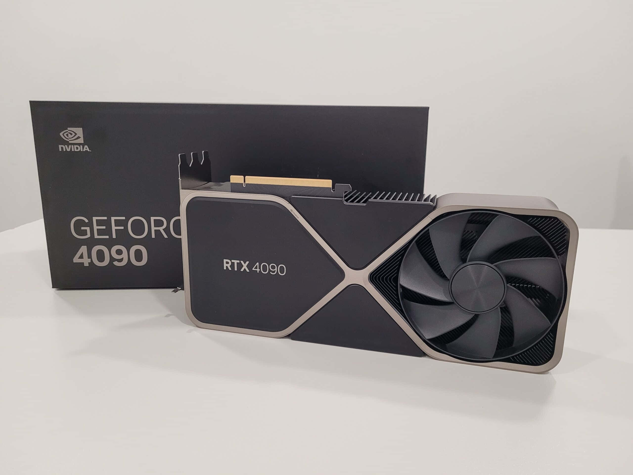 nvidia 桌布 壁紙 — 一張時尚的黑色NVIDIA GeForce RTX 4090顯示卡，帶有銀色點綴，放在白色表面上，旁邊是其匹配的盒子。