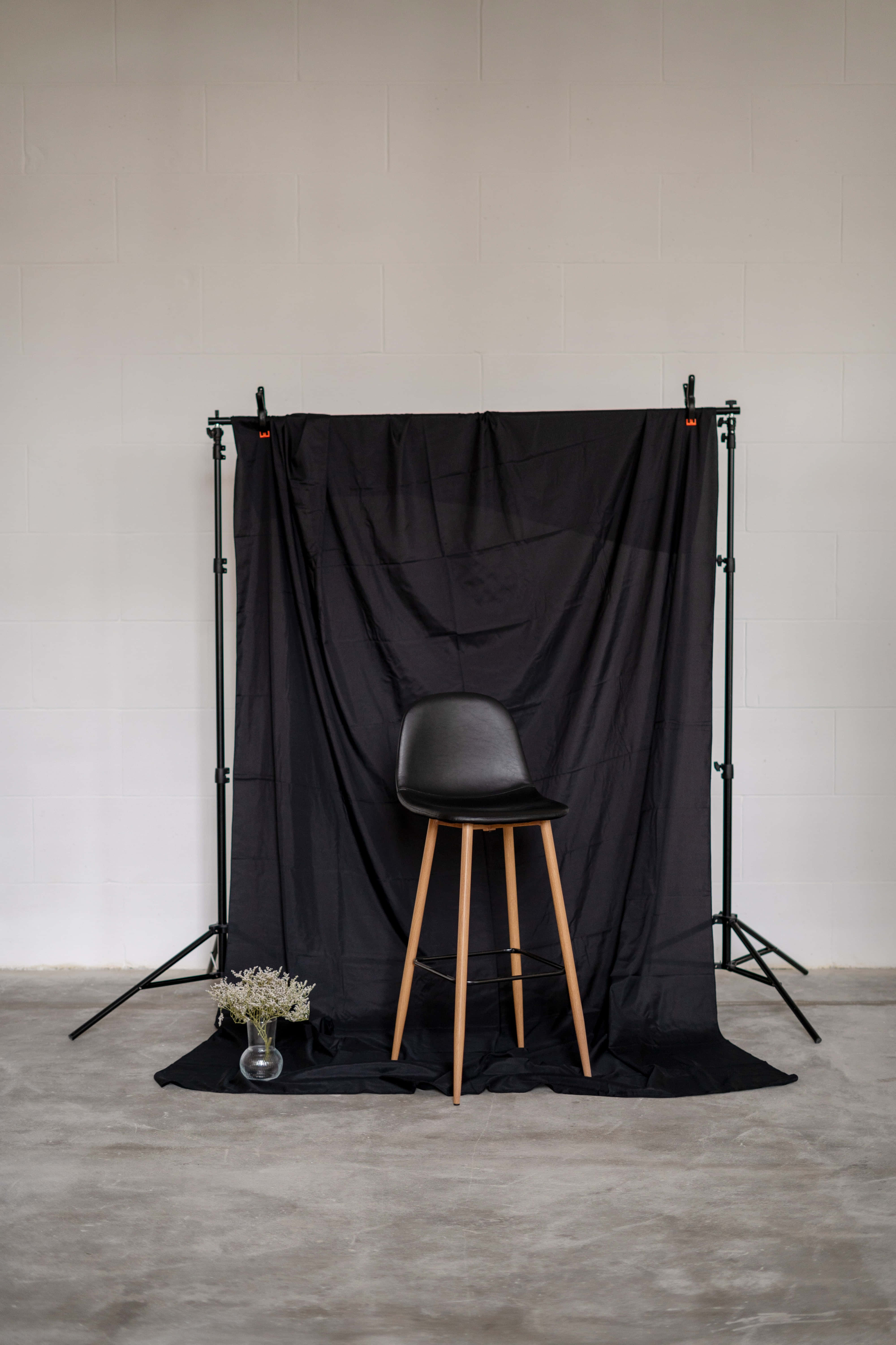 Photography Studio 桌布 壁紙 — 一張時尚的黑色凳子搭配木腿，置中放在極簡風格工作室空間的黑色布幕前。