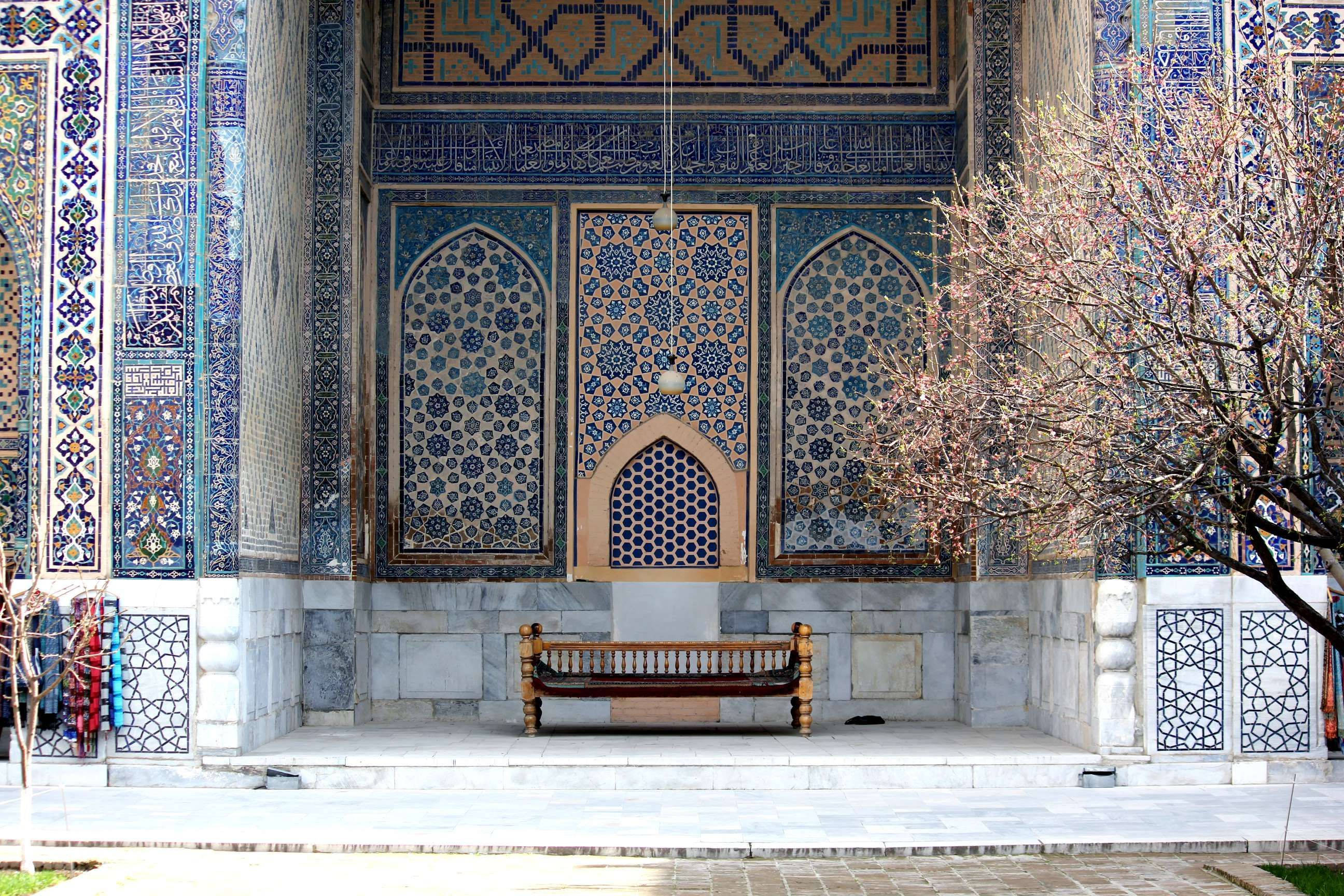 Uzbekistan 桌布 壁紙 — 一張木凳放在一個裝飾華麗的藍金瓷磚伊斯蘭聖殿前，帶有複雜的幾何圖案和拱形壁龕。