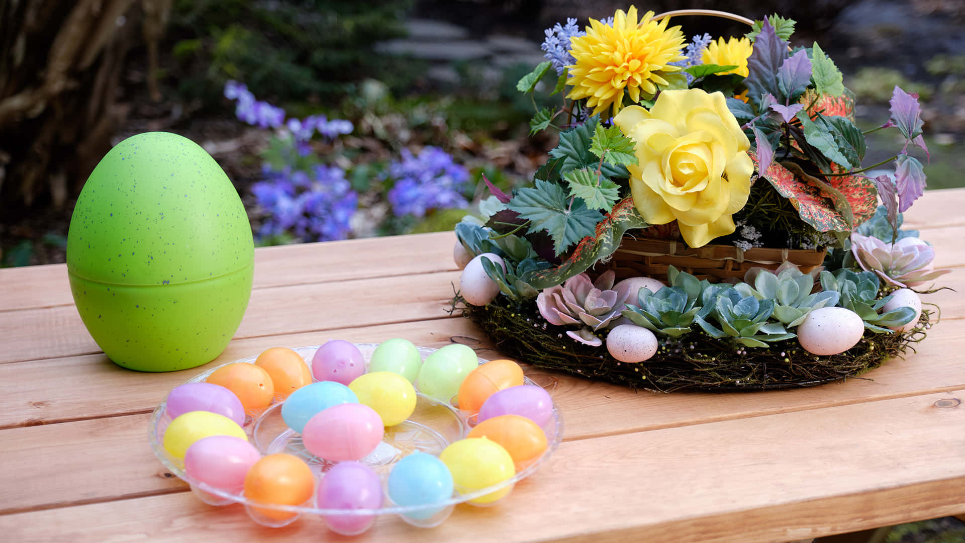 Easter Zoom 桌布 壁紙 — 一張木桌上展示了一個綠色斑點的復活節蛋、一盤色彩繽紛的塑膠蛋，以及一個由黃玫瑰和多肉植物組成的花環。