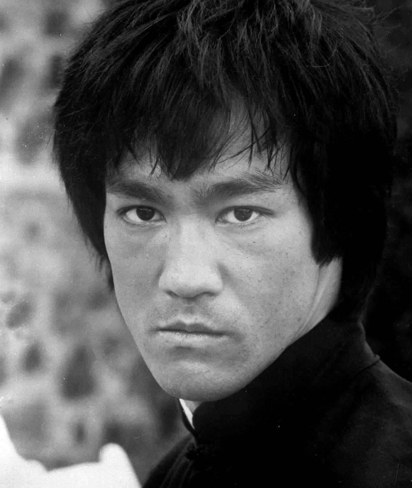 李小龍 桌布 壁紙 — 一張李小龍的黑白特寫肖像，眼神凌厲，頭髮凌亂，背景模糊。