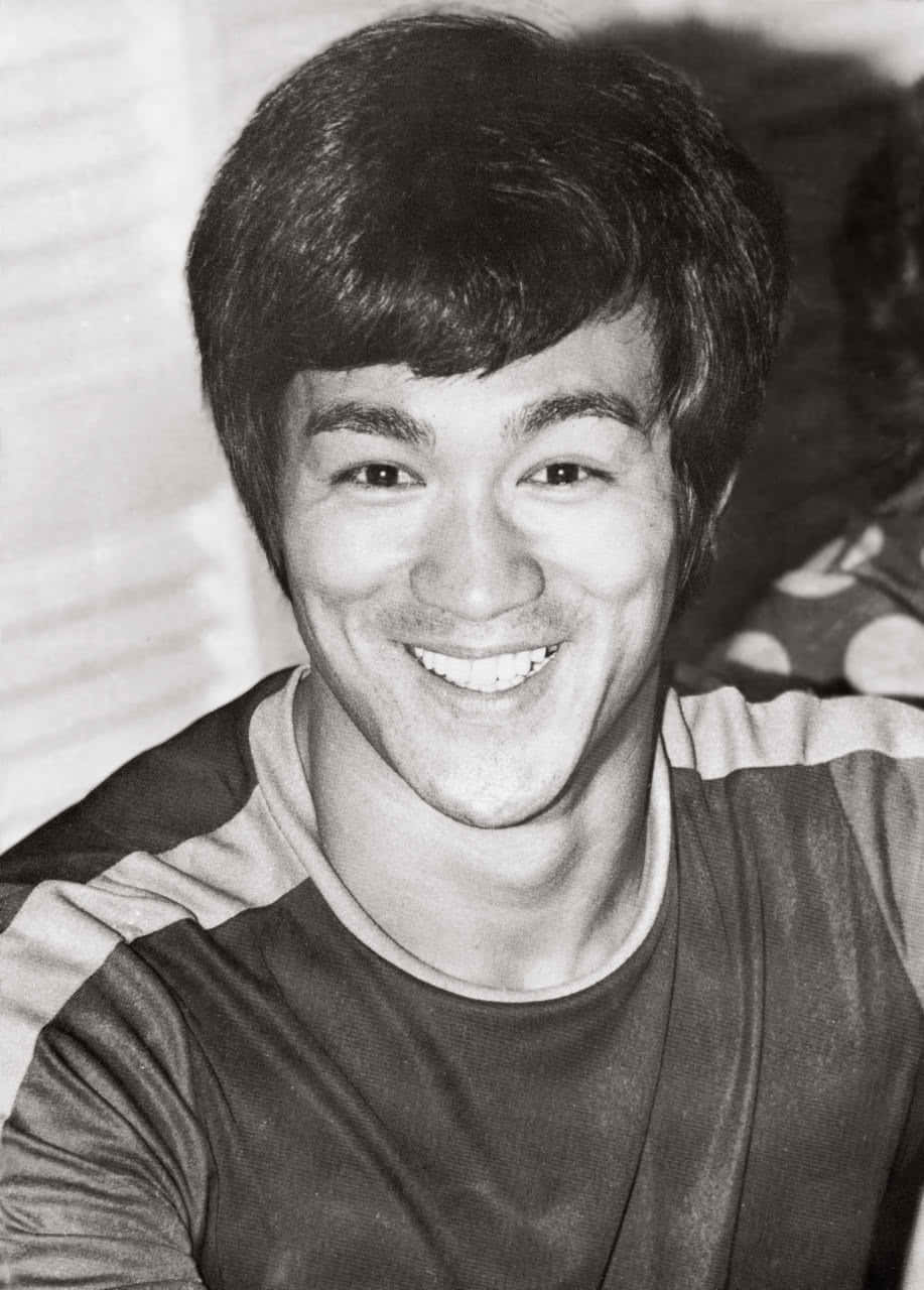 李小龍 桌布 壁紙 — 一張李小龍的黑白近距離肖像，他頭髮蓬鬆，穿著條紋襯衫，對著鏡頭溫暖微笑。