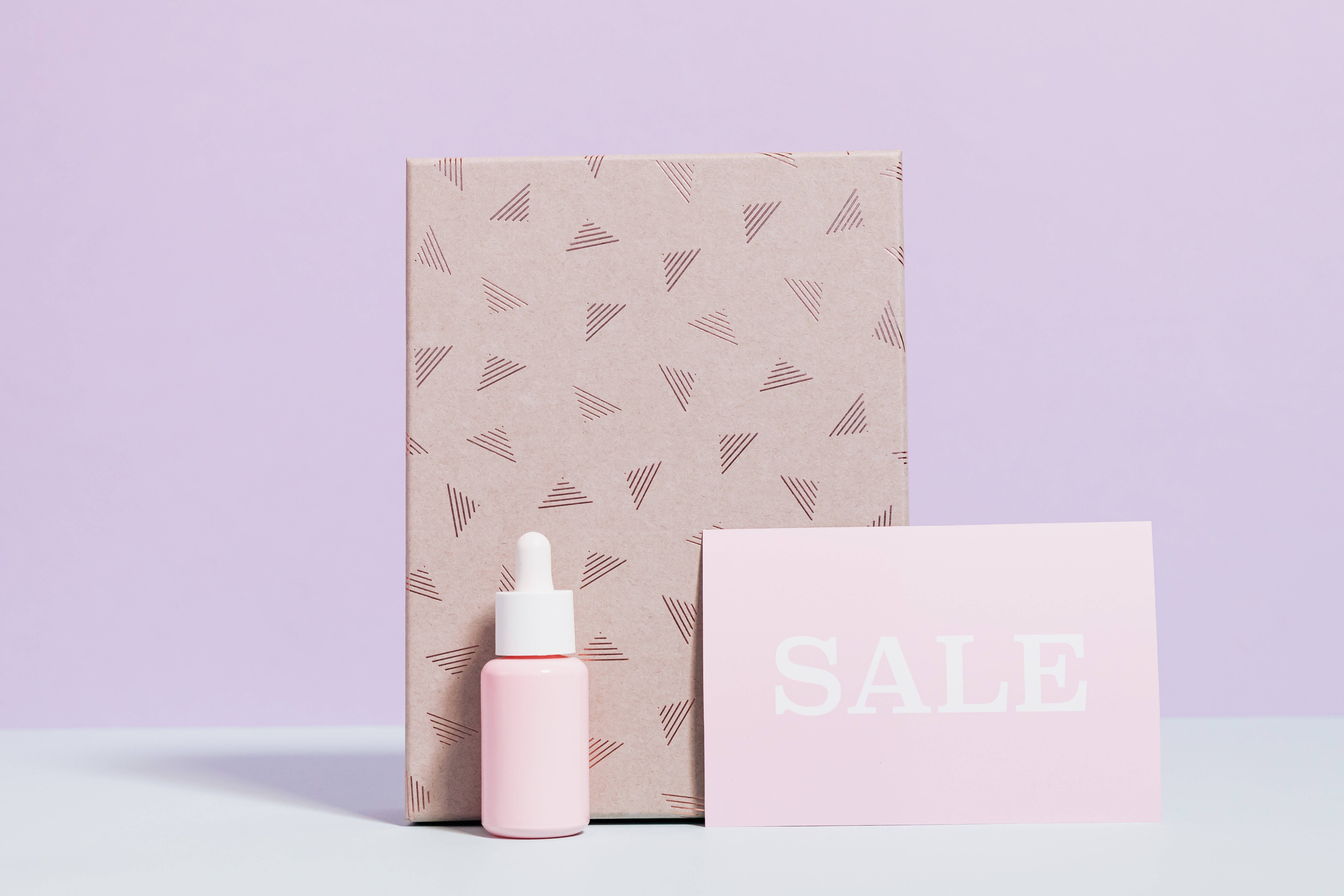Cute Pastel Aesthetic 桌布 壁紙 — 一張極簡風格的產品照，以柔和薰衣草背景襯托粉紅色滴管瓶、圖案盒子和特價卡。