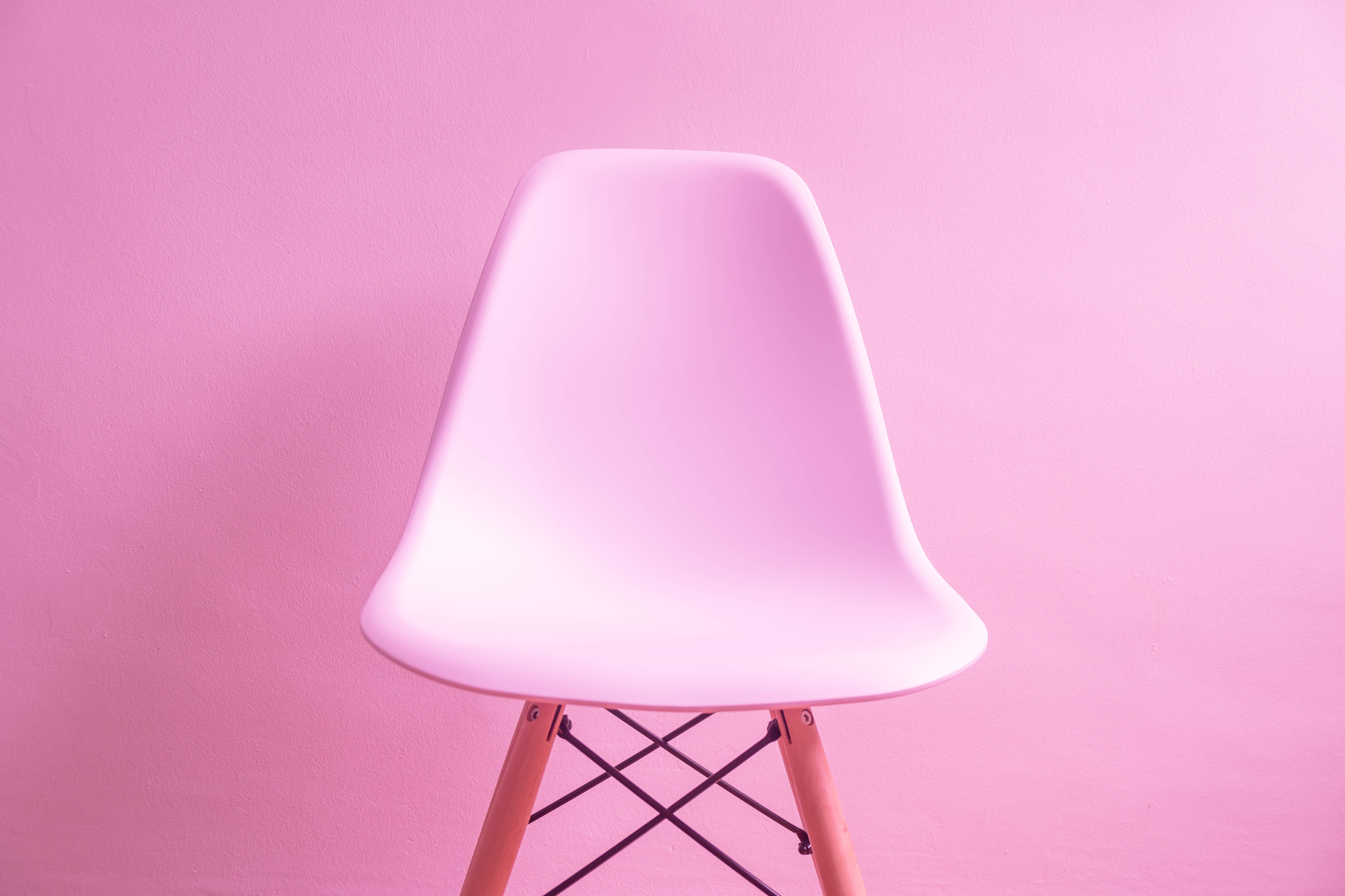 粉紅色 桌布 壁紙 — 一張極簡風格的粉紅色模塑膠椅，配以木腳，靠著純粉紅色牆壁。