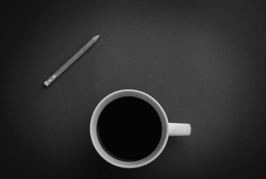 Black Coffee 桌布 壁紙 — 一張極簡黑白俯拍照片，拍攝白色咖啡杯和鉛筆放在深色紋理表面上。