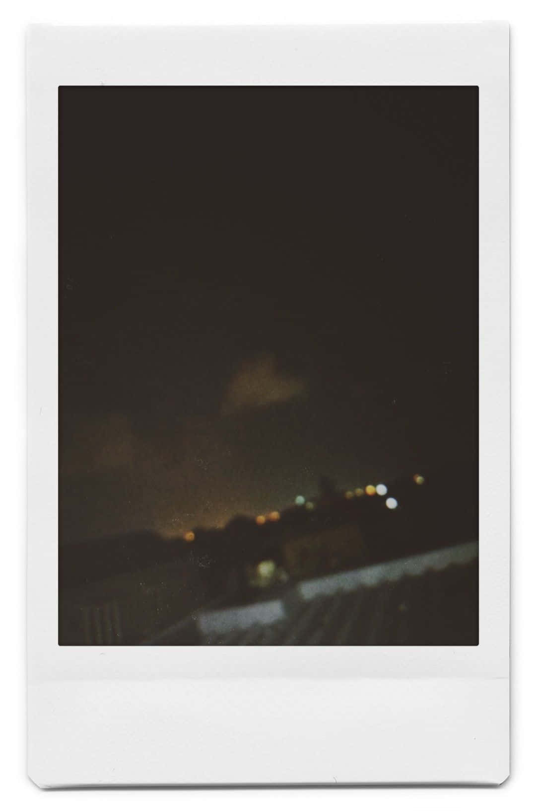 Aesthetic Polaroid 桌布 壁紙 — 一張模糊的拍立得格式夜景照片，顯示在黑暗天空和淡淡雲層襯托下的遠處城市燈光。
