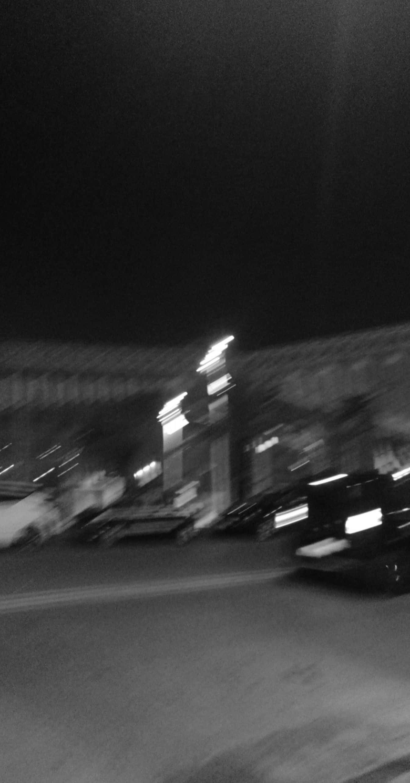 黑白 桌布 壁紙 — 一張模糊的黑白夜間照片，捕捉汽車和街燈在運動中掠過的瞬間。
