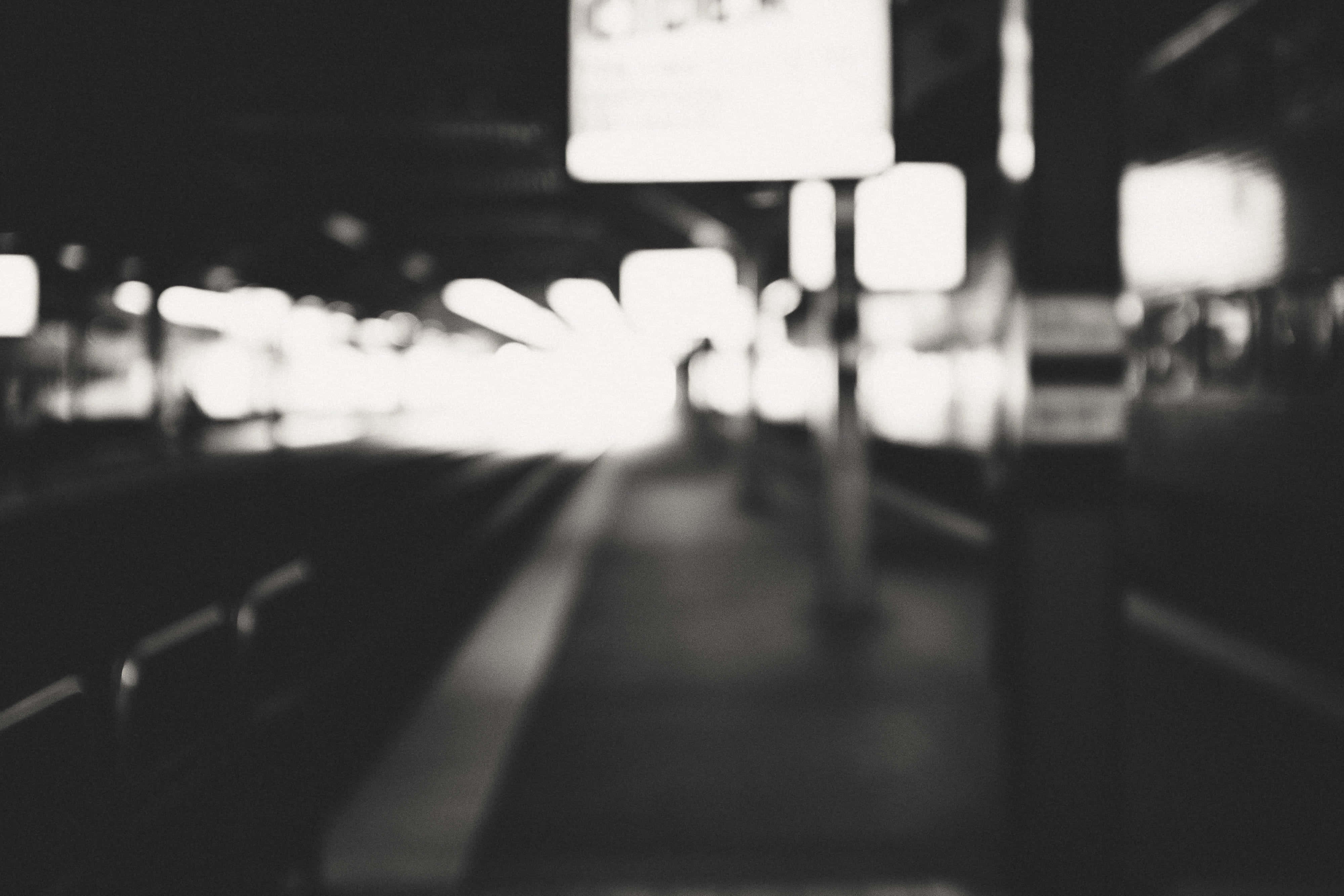 Black And White City 桌布 壁紙 — 一張模糊的黑白照片，拍攝夜晚的火車站月台，帶有發光的燈光和模糊不清的形狀。