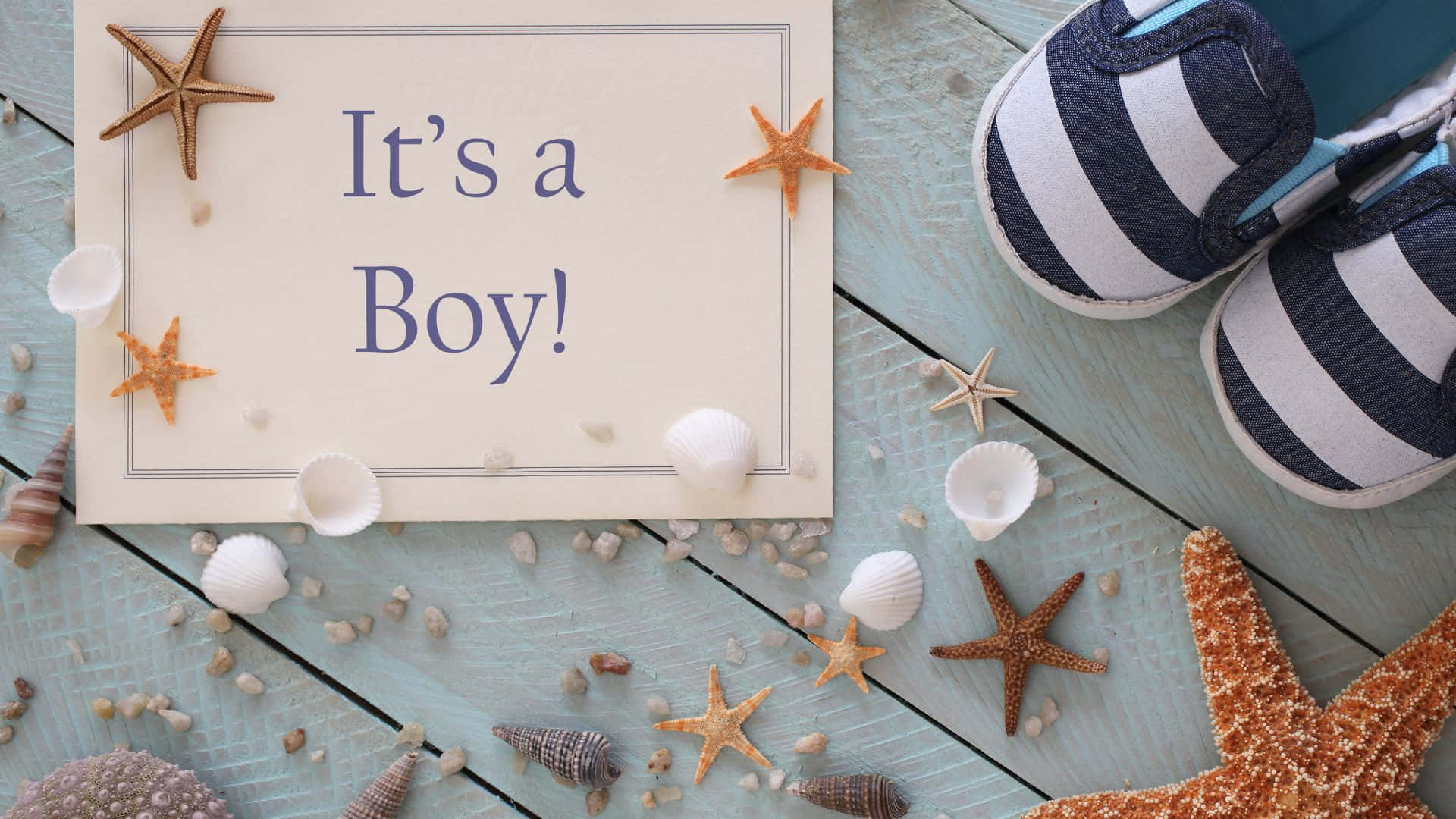 Boy 桌布 壁紙 — 一張歡樂的公告卡，上面寫著「It's a Boy!」，周圍環繞著海星、貝殼和嬰兒鞋，放置在經風化的藍色木質表面上。