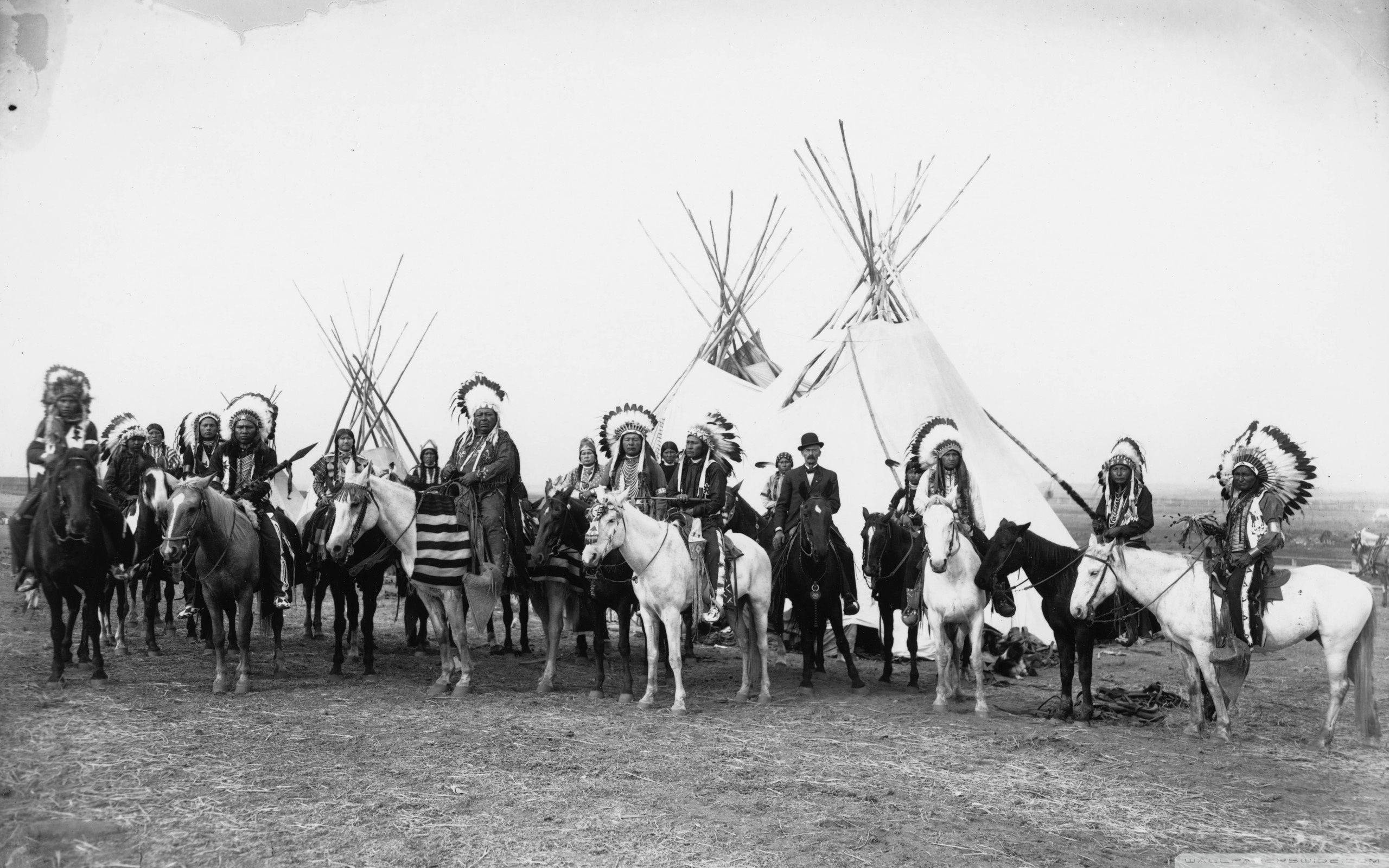 Native American 桌布 壁紙 — 一張歷史黑白照片，顯示美洲原住民騎手戴著頭飾，在開闊平原的帳篷附近與馬匹合影。