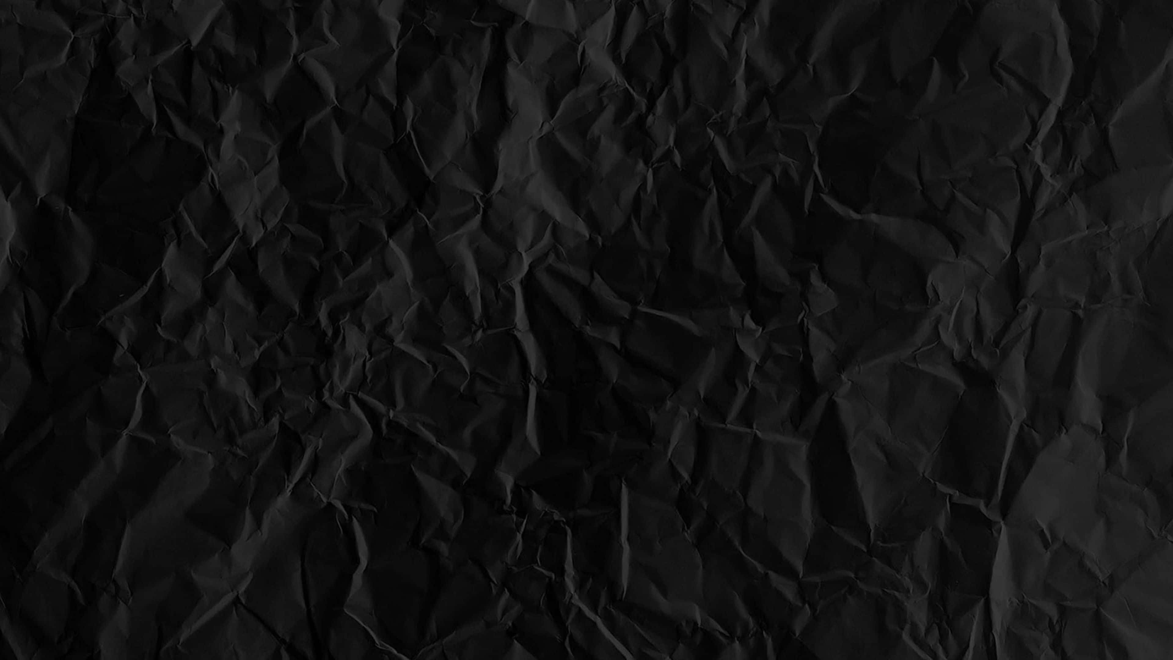 texture 桌布 壁紙 — 一張深度皺摺的黑色紙張特寫，帶有紋理摺痕和細微陰影，營造出陰鬱的抽象表面。