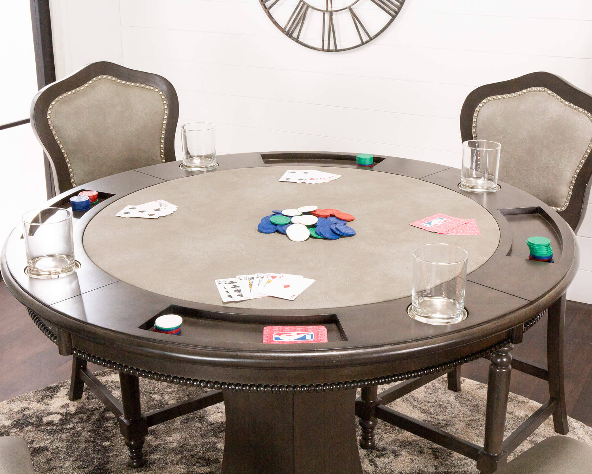 Poker 桌布 壁紙 — 一張深色木製撲克桌，上面散落著紙牌和彩色籌碼，在一個現代化的房間裡，配有椅子和掛鐘，準備好進行遊戲。