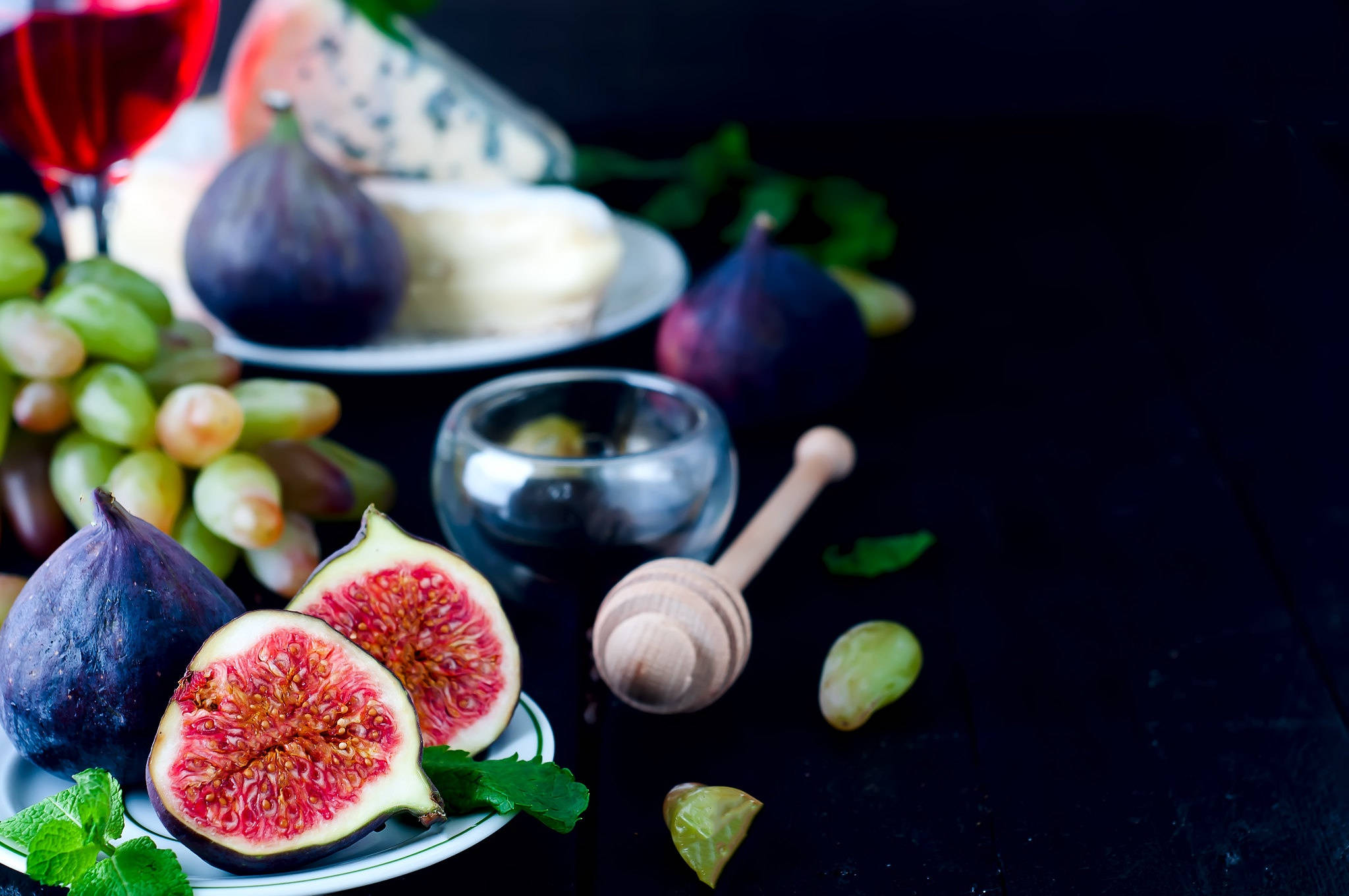 Fruits 桌布 壁紙 — 一張深色鄉村風格的桌子上擺放著切片無花果、葡萄、起司和蜂蜜，配上一杯紅酒，營造出優雅的美食靜物畫面。