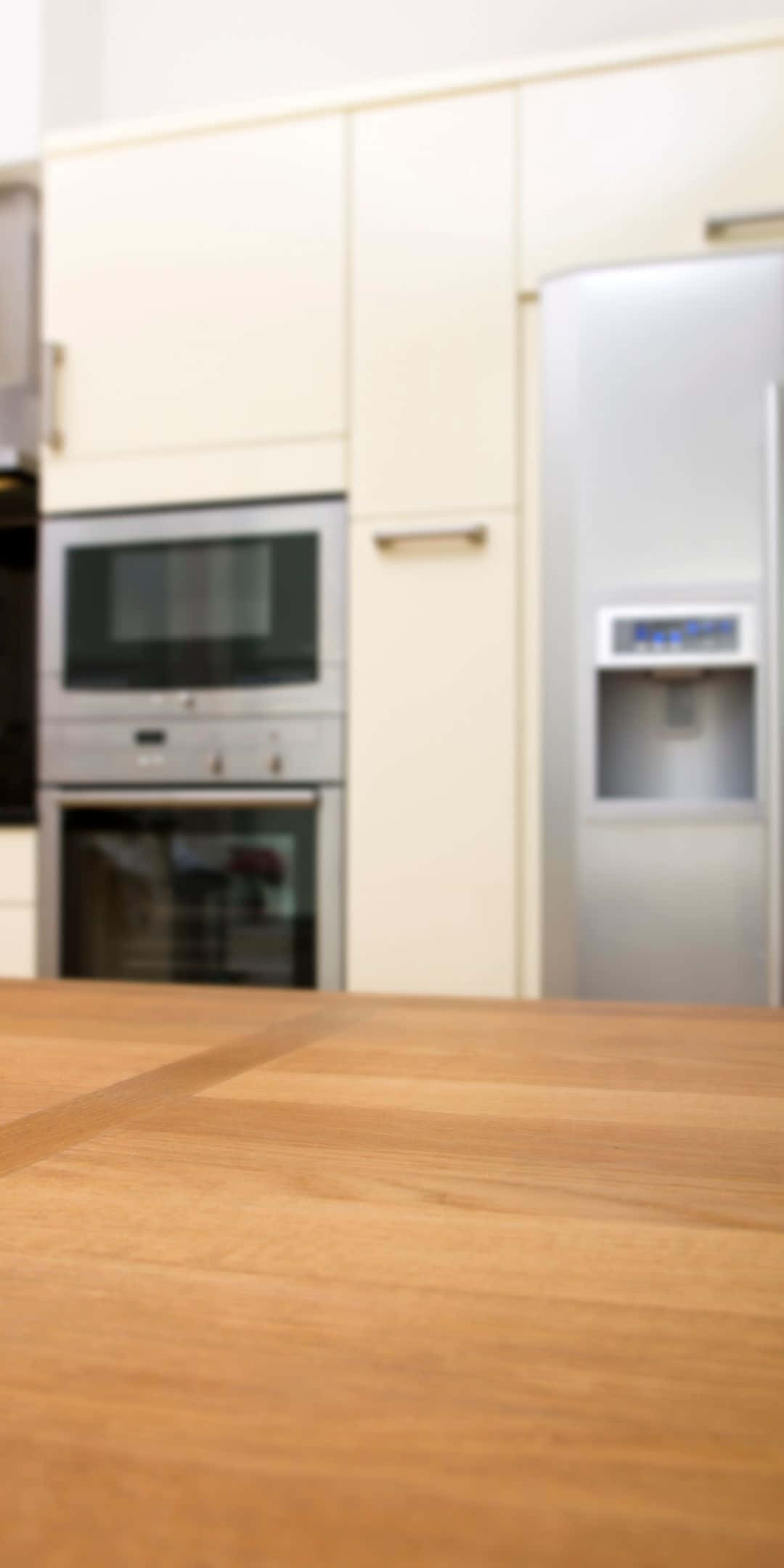 Pixel 3 Kitchen 桌布 壁紙 — 一張淺景深照片，聚焦於溫暖的木製檯面，背景中的現代廚房電器模糊不清。