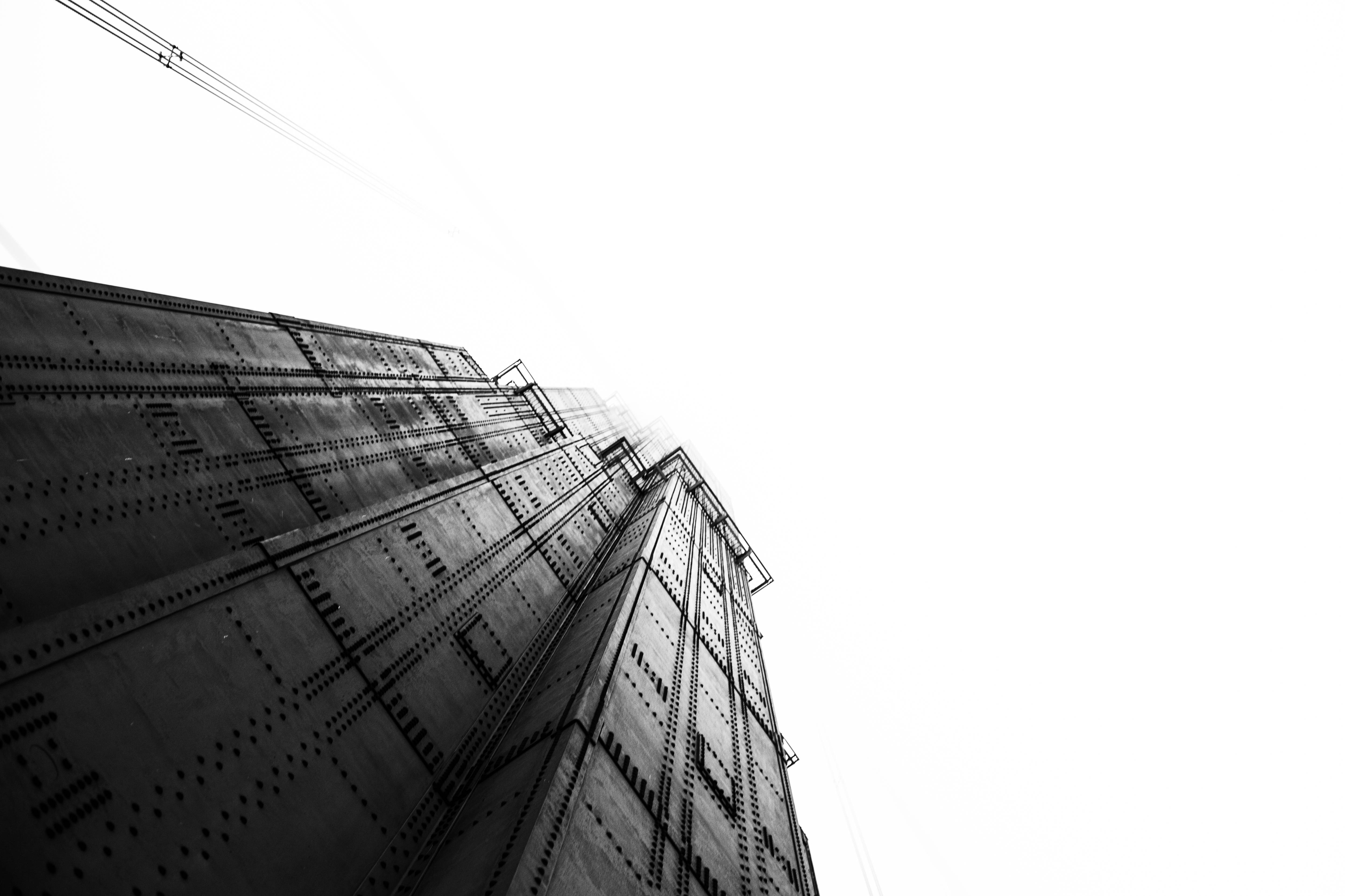 4K 白色 桌布 壁紙 — 一張清晰的黑白低角度照片，拍攝了一座鉚接的工業塔穿透明亮的陰天。