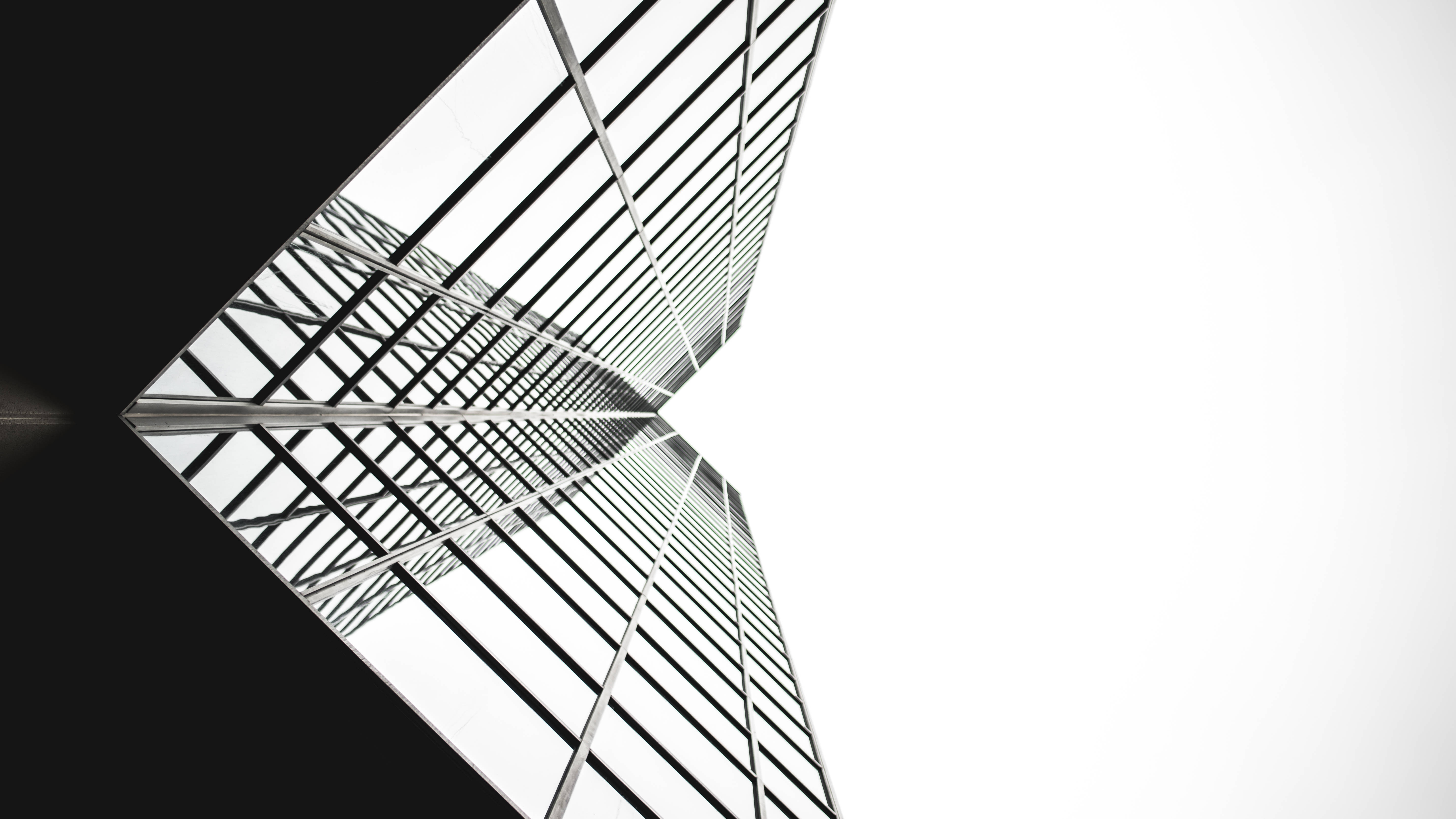 建築 桌布 壁紙 — 一張清晰的黑白低角度照片，現代玻璃摩天大樓的幾何網格向明亮的天空匯聚。