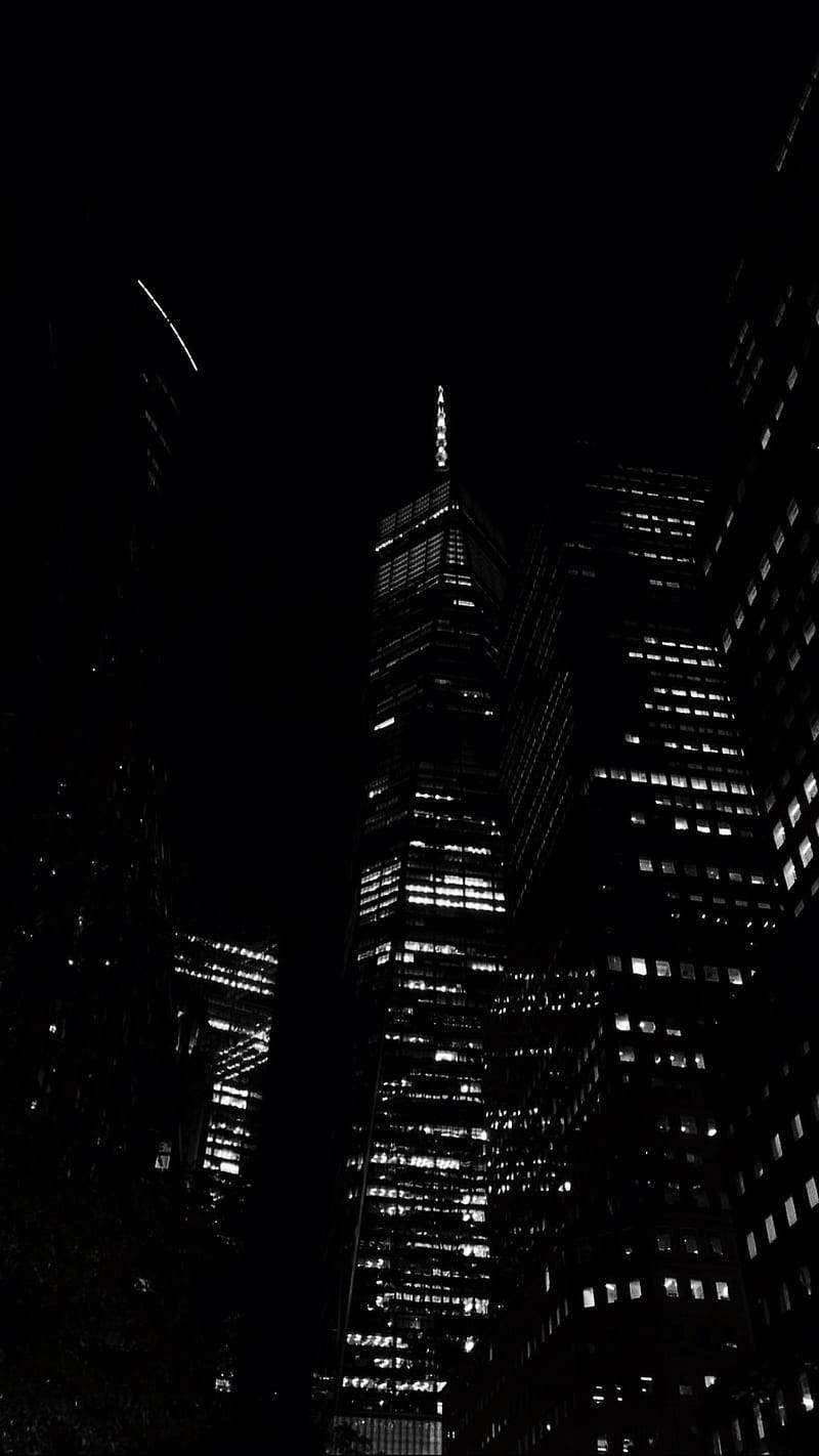 黑夜 桌布 壁紙 — 一張清晰的黑白夜景照片，高聳的摩天大樓以發光的窗戶刺穿黑暗的天空。