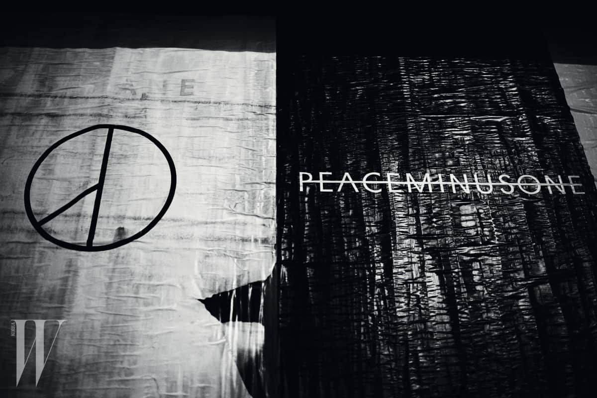peaceminusone 桌布 壁紙 — 一張清晰的黑白照片，在戲劇性燈光下，紋理布料上顯示和平符號和「PEACEMINUSONE」文字。