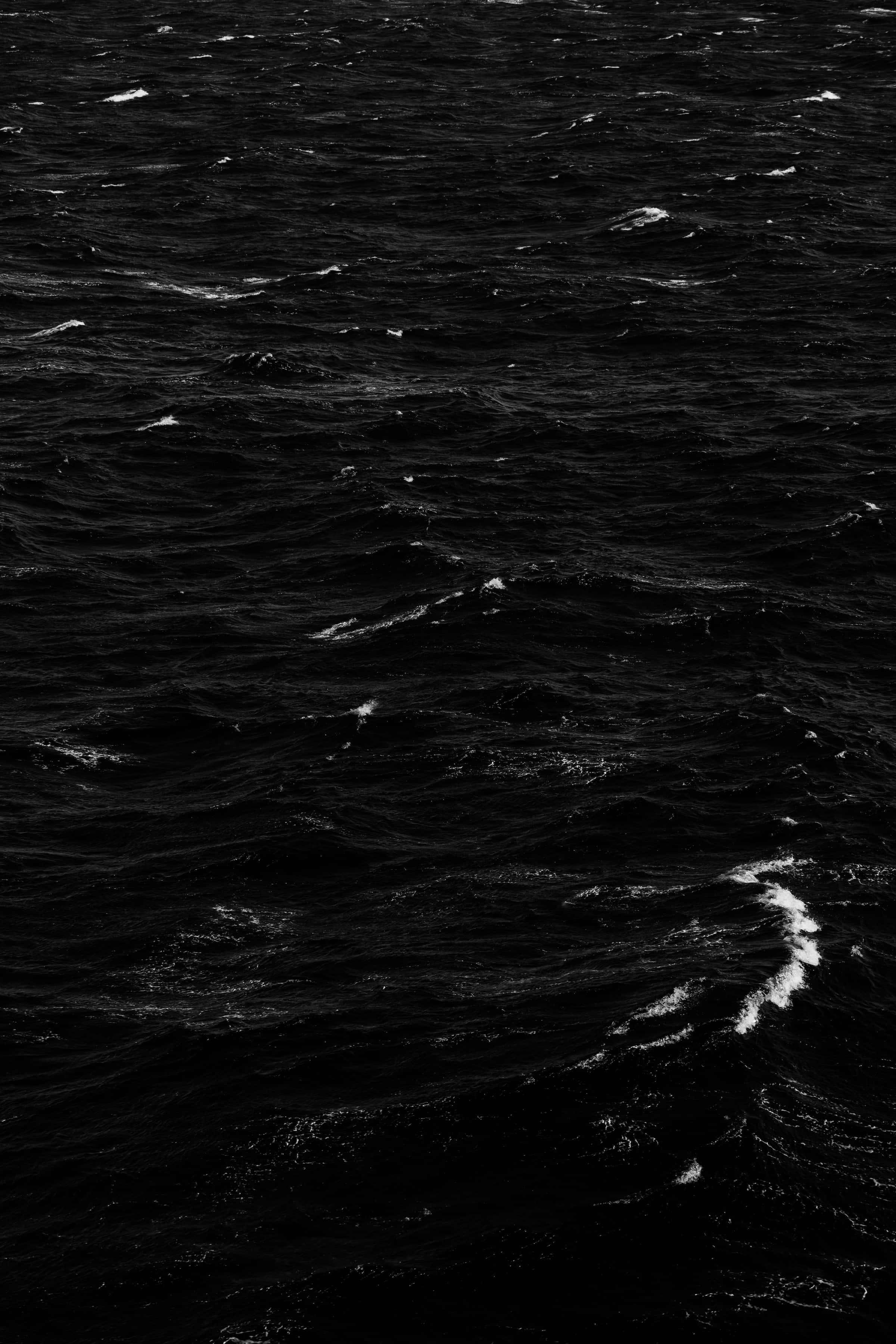 Black And White Ocean 桌布 壁紙 — 一張清晰的黑白照片，拍攝了洶湧的海浪，白色泡沫在黑暗的海面上翻騰。
