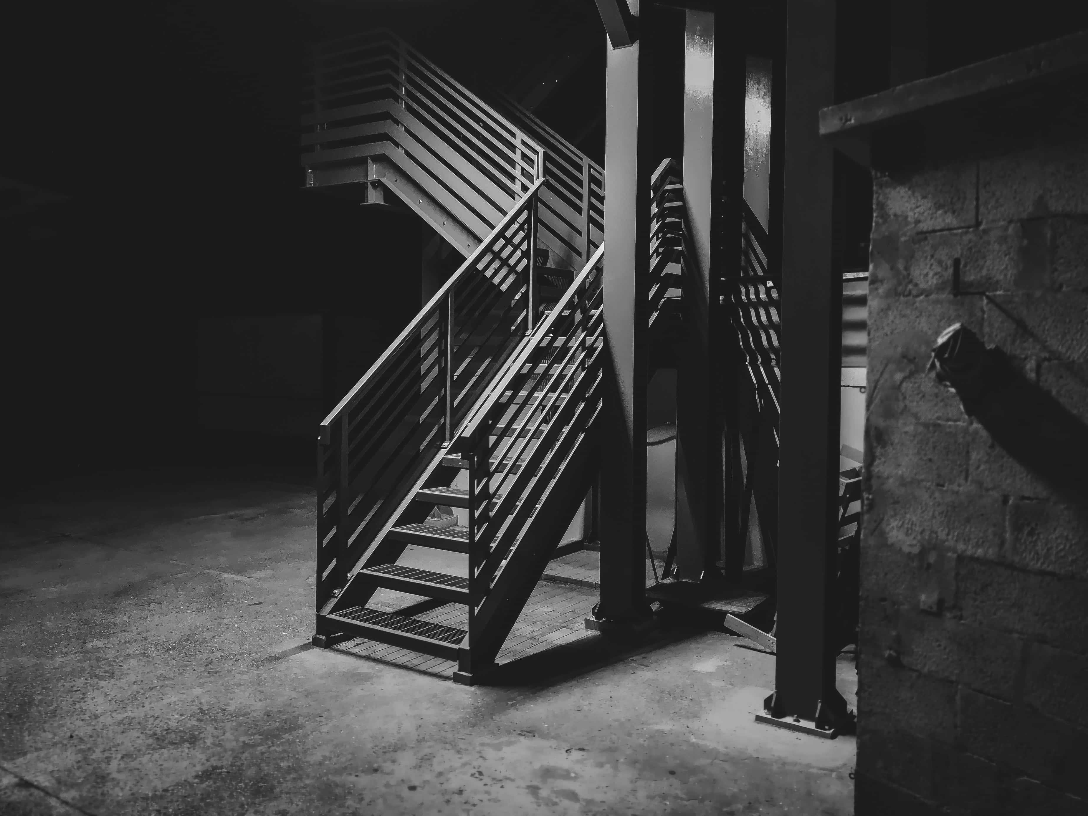 Underground 桌布 壁紙 — 一張清晰的黑白照片，拍攝工業金屬樓梯沿著粗糙的磚牆向上延伸至陰影黑暗之中。