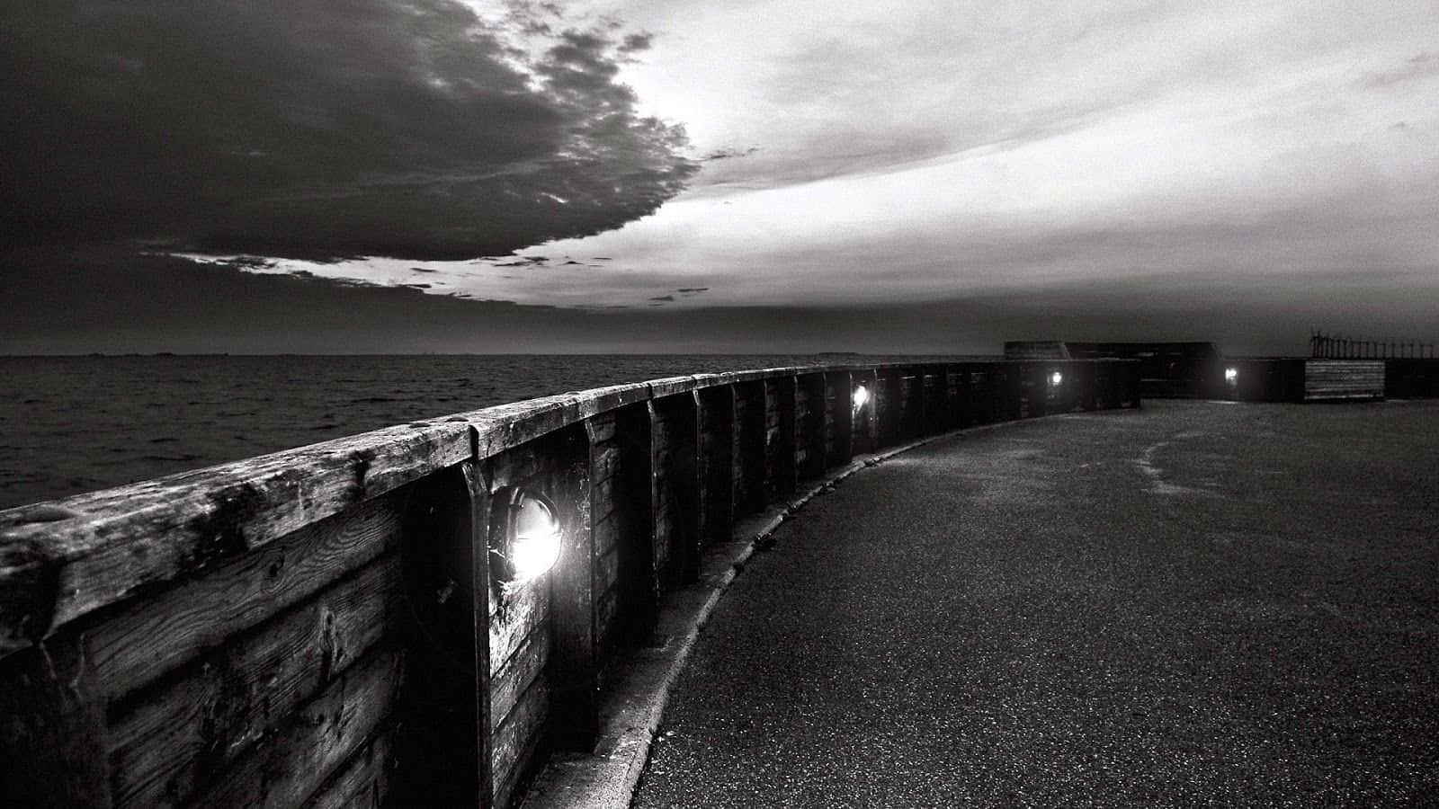 Black And White Landscape 桌布 壁紙 — 一張清晰的黑白照片，拍攝於黃昏時分，彎曲的碼頭上有發光的燈籠，背景是戲劇性的多雲天空。