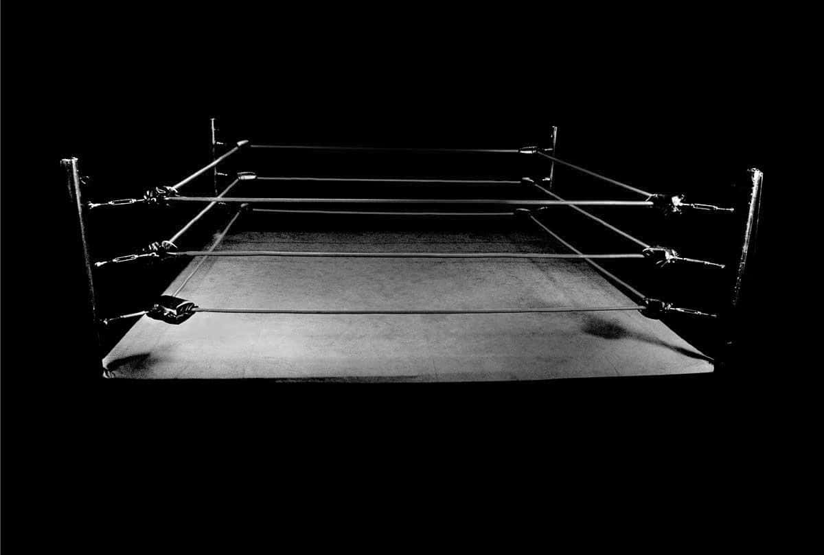 Wrestling Ring 桌布 壁紙 — 一張清晰的黑白照片，空蕩蕩的摔角擂台在漆黑背景中照亮。