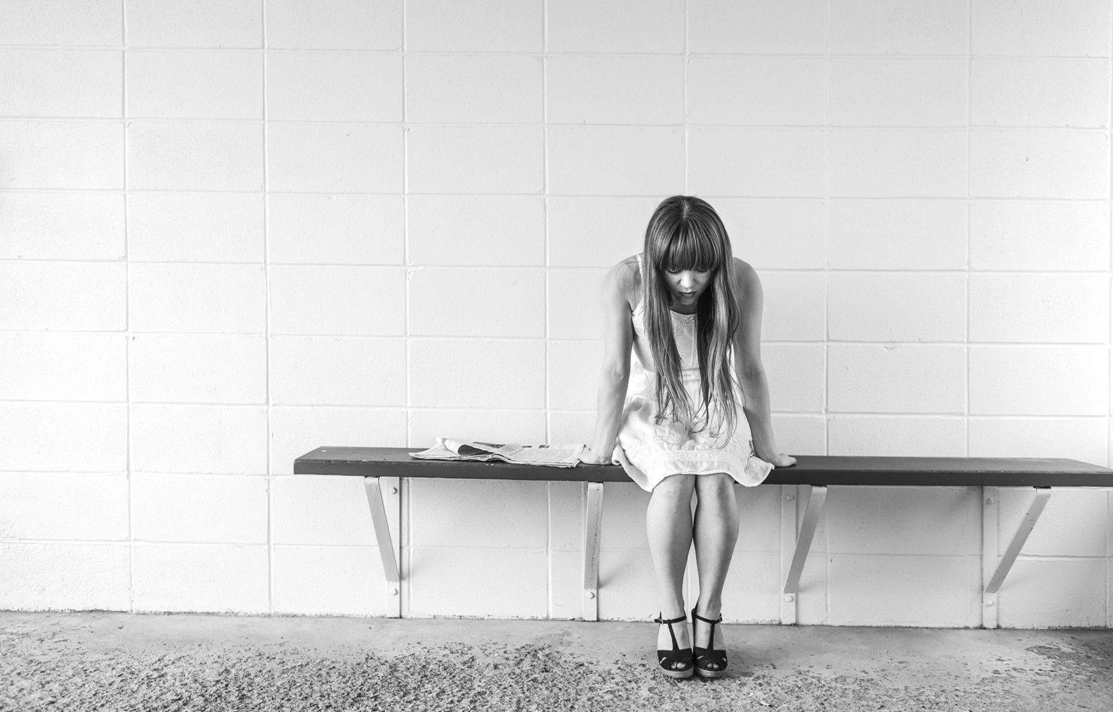 Single Girl 桌布 壁紙 — 一張清晰的黑白照片中，一名年輕女子癱坐在長椅上，背景是樸素的瓷磚牆。