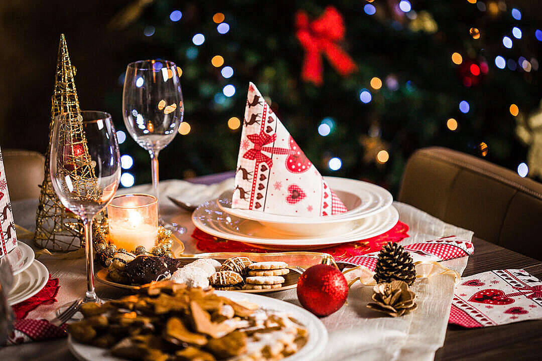 Pretty Christmas 桌布 壁紙 — 一張溫暖照明的聖誕餐桌，擺放著節日餐盤、餅乾、松果，背景是閃爍的聖誕樹燈。